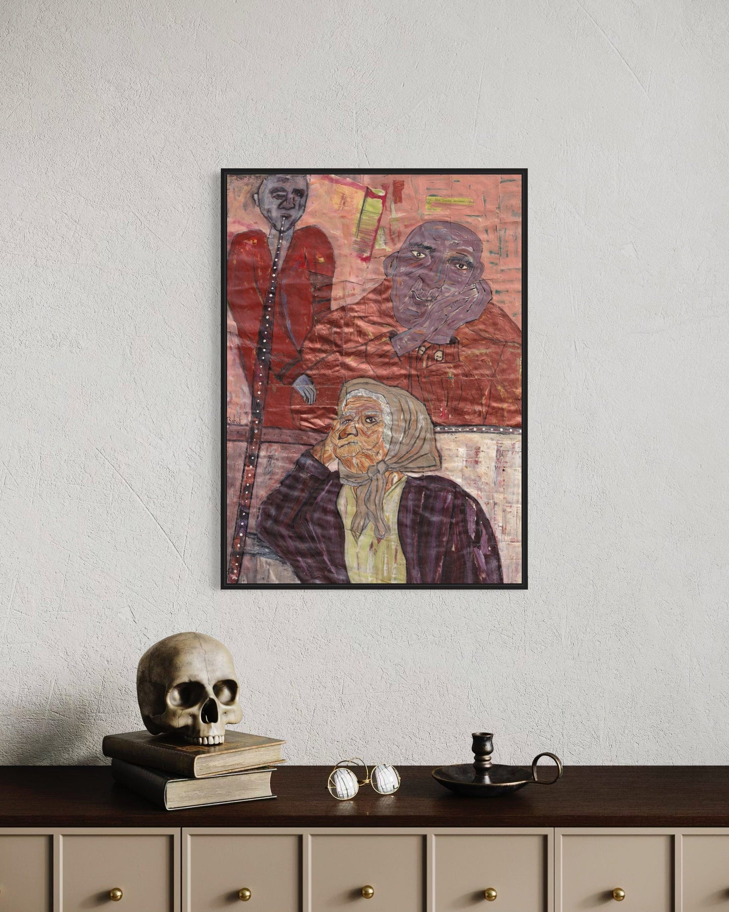 Framed artwork of three figures on a wall above a shelf with decorative items.