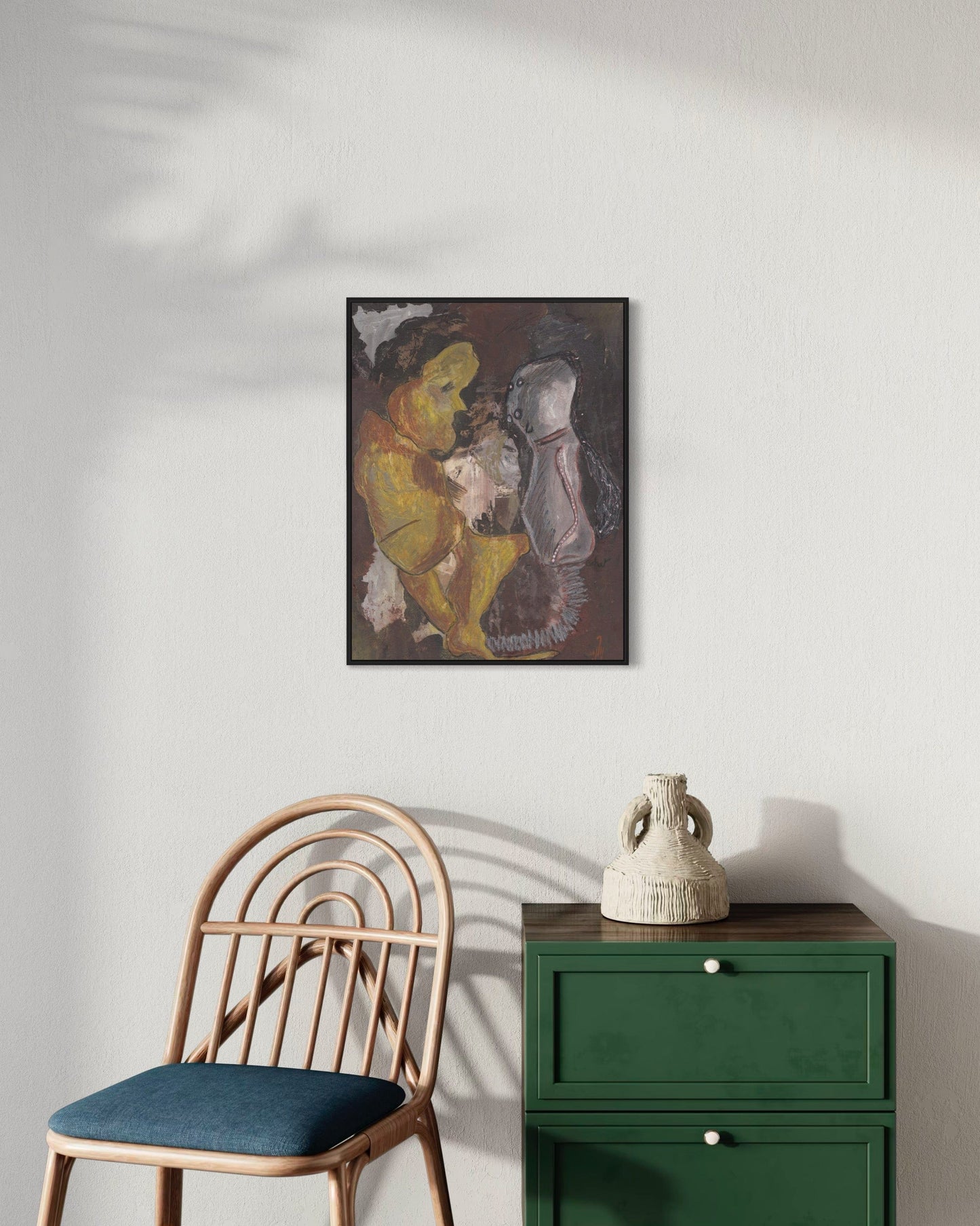Framed artwork on a wall above a green cabinet and wooden chair.
