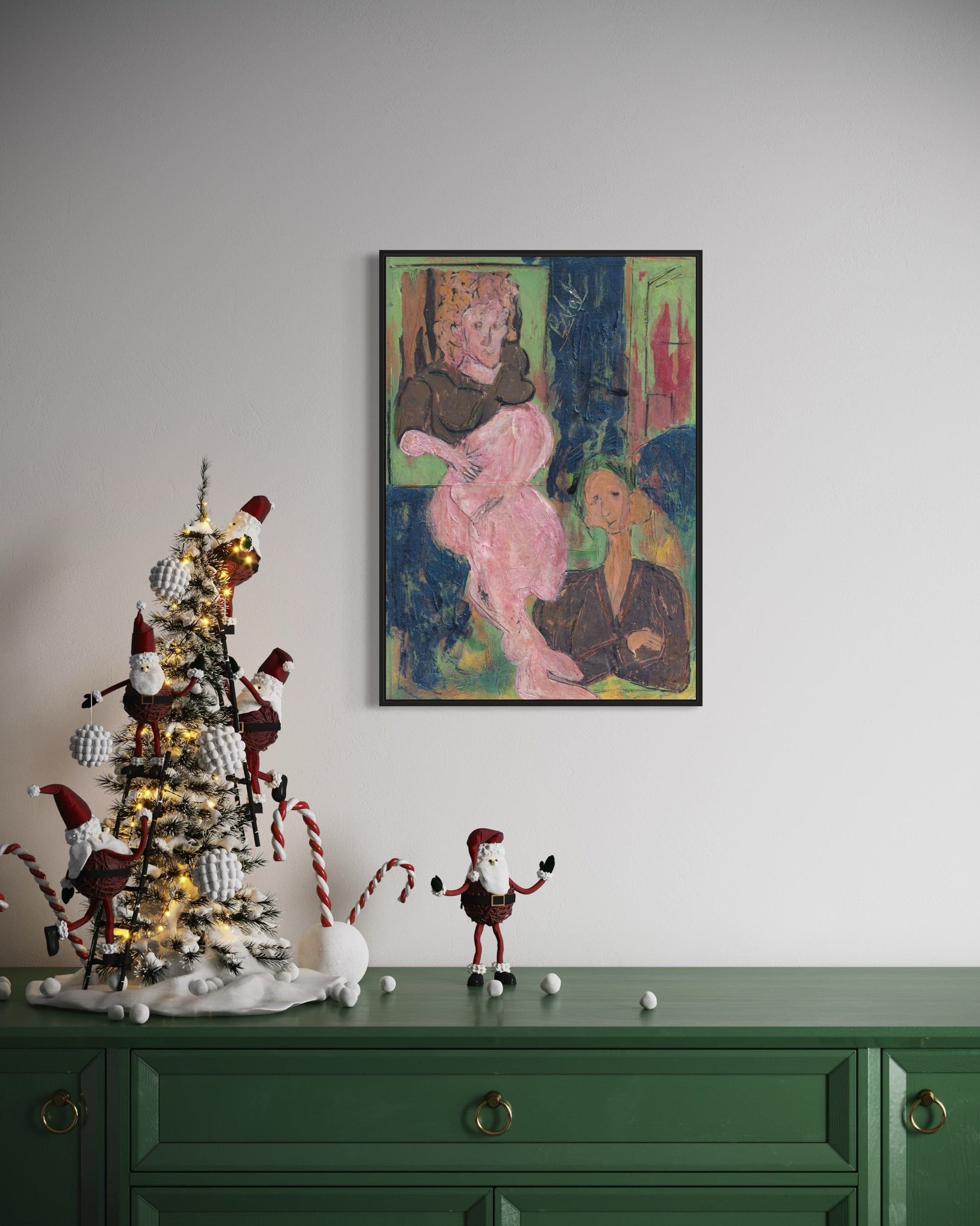 Decorative Christmas tree with ornaments on a green cabinet, framed artwork on the wall.