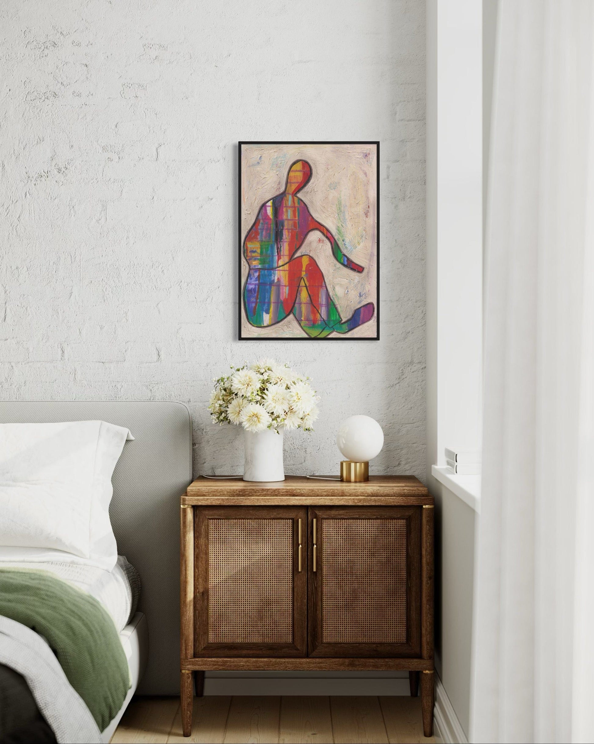 Colorful abstract painting on a wall above a wooden cabinet with flowers and a lamp.