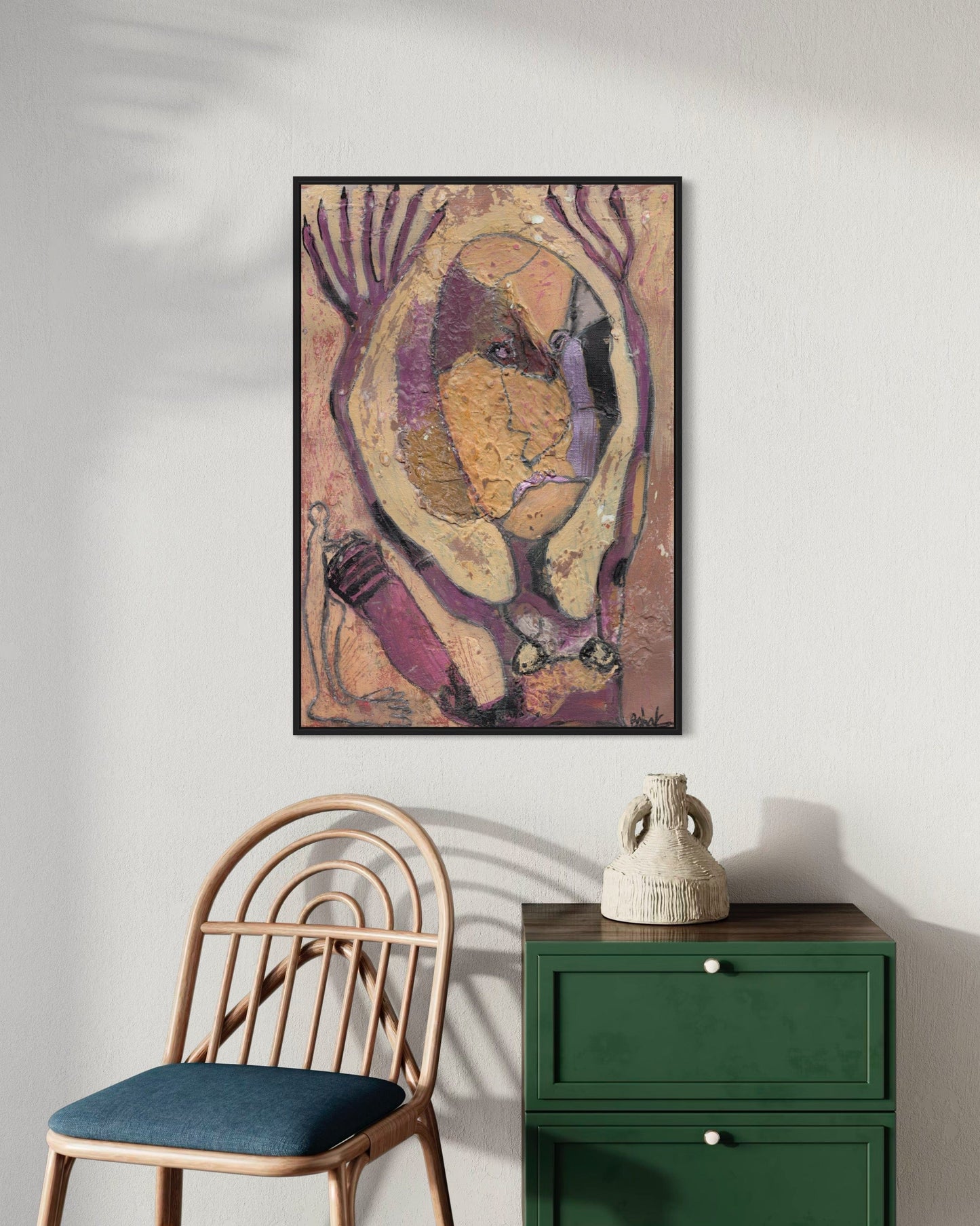 Framed abstract art piece on a wall above a chair and green cabinet.