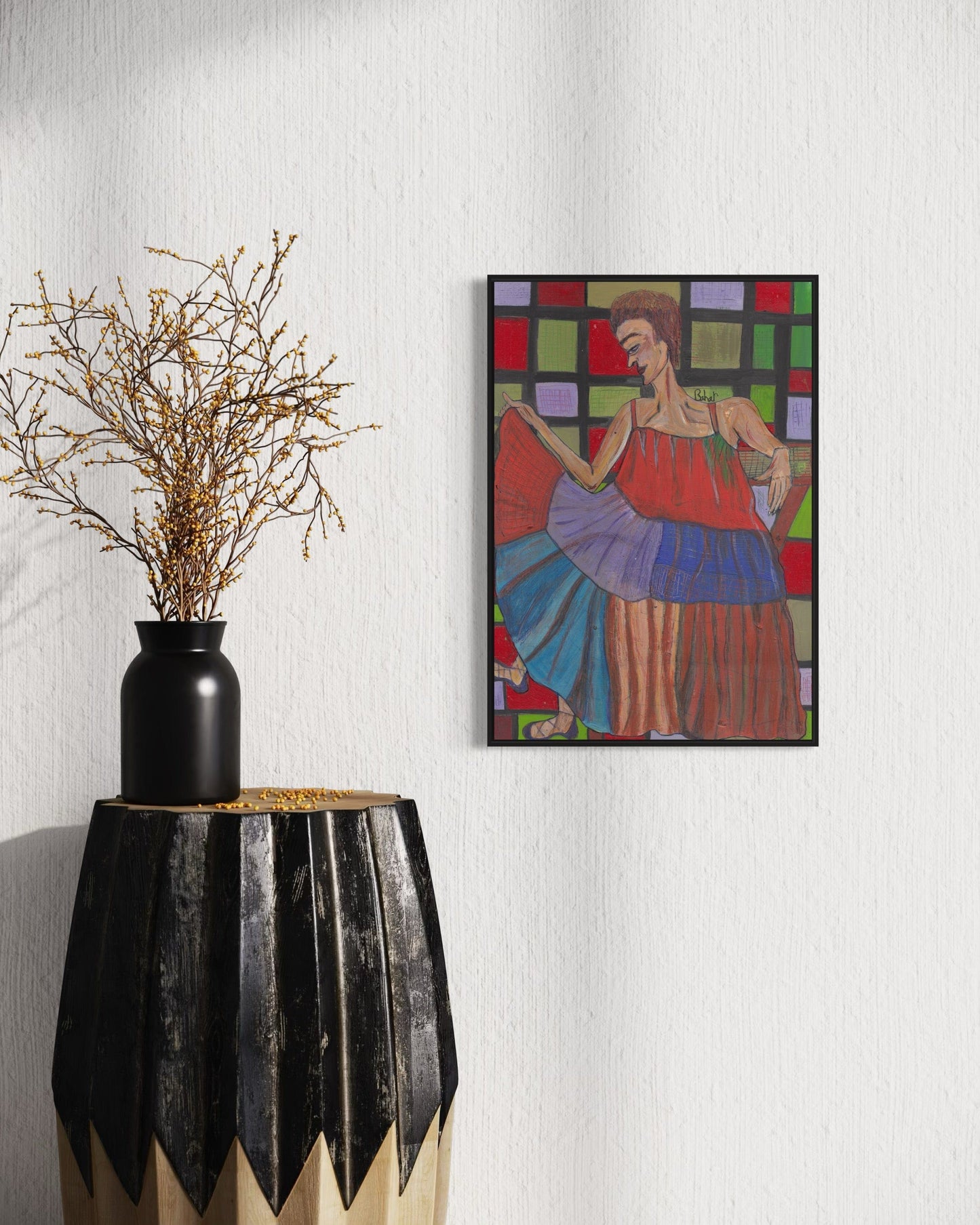 Framed abstract painting on a wall next to a black vase with branches.
