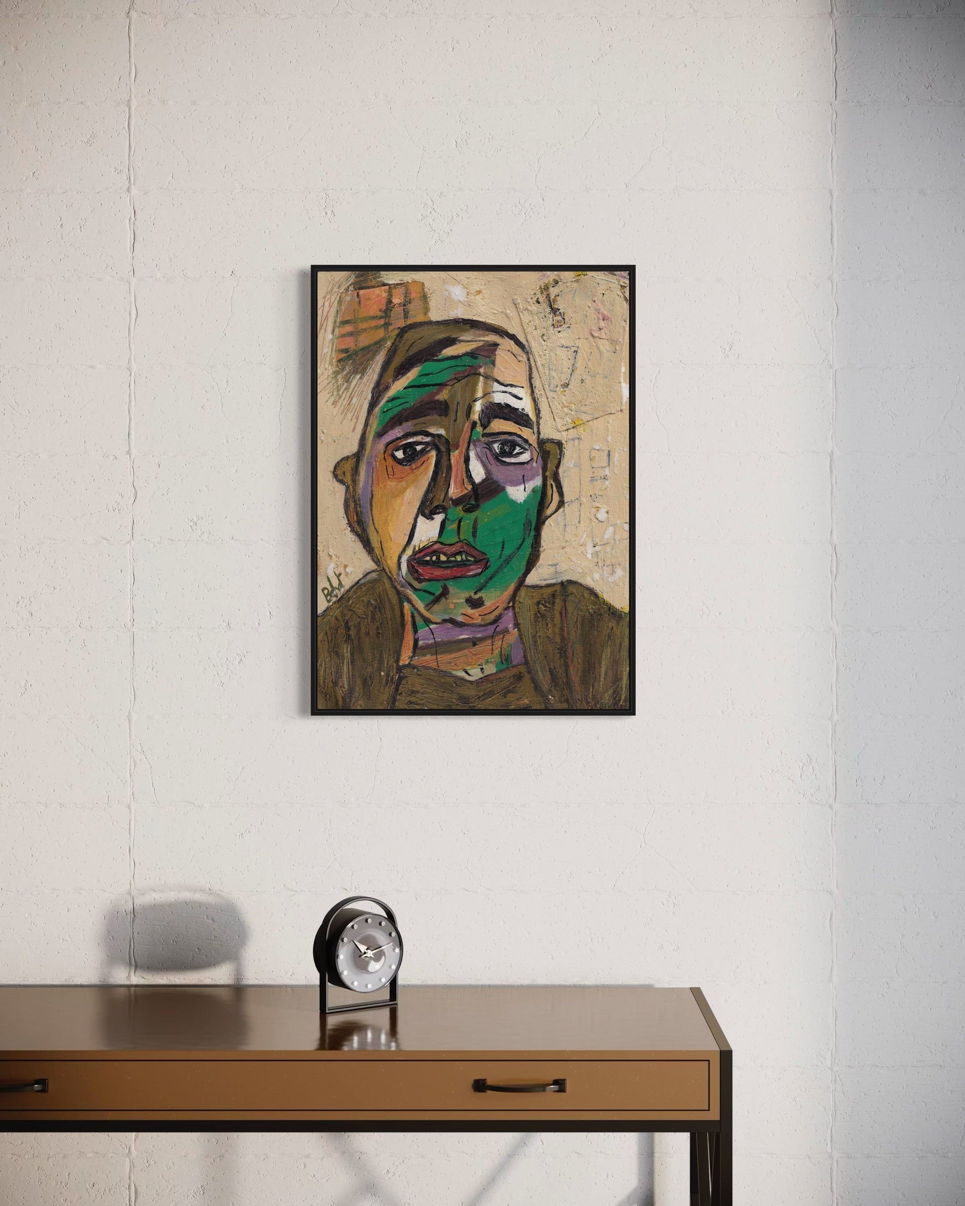 Framed abstract portrait on a wall above a desk with a clock.