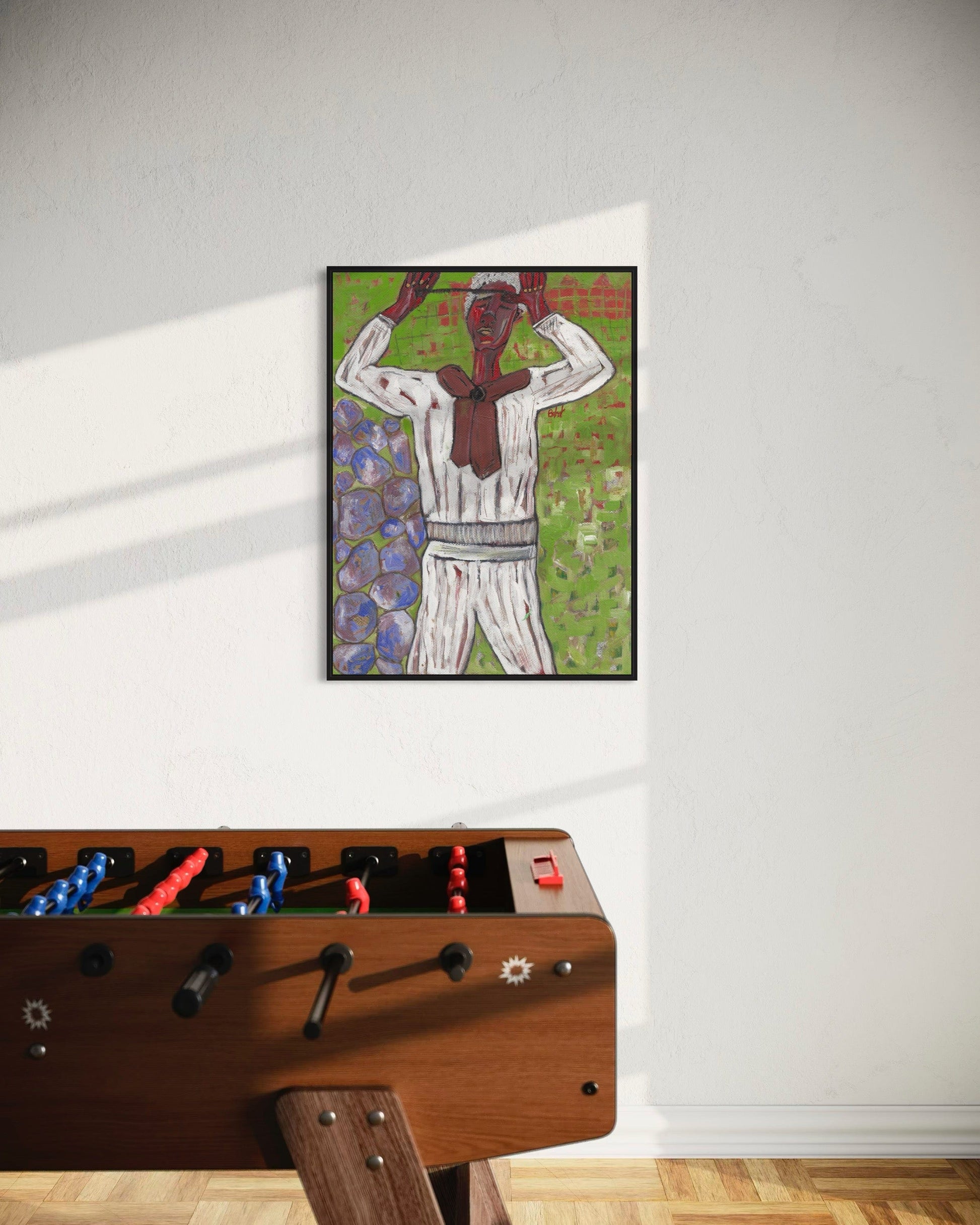 Framed artwork of a person in a white shirt and pants on a wall above a foosball table.