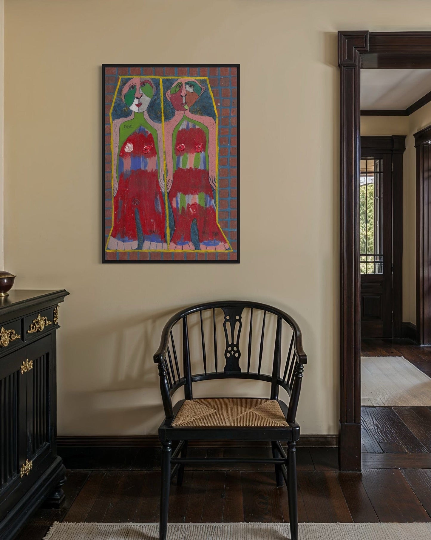 Colorful abstract painting on a wall above a black chair in a room with wooden flooring.