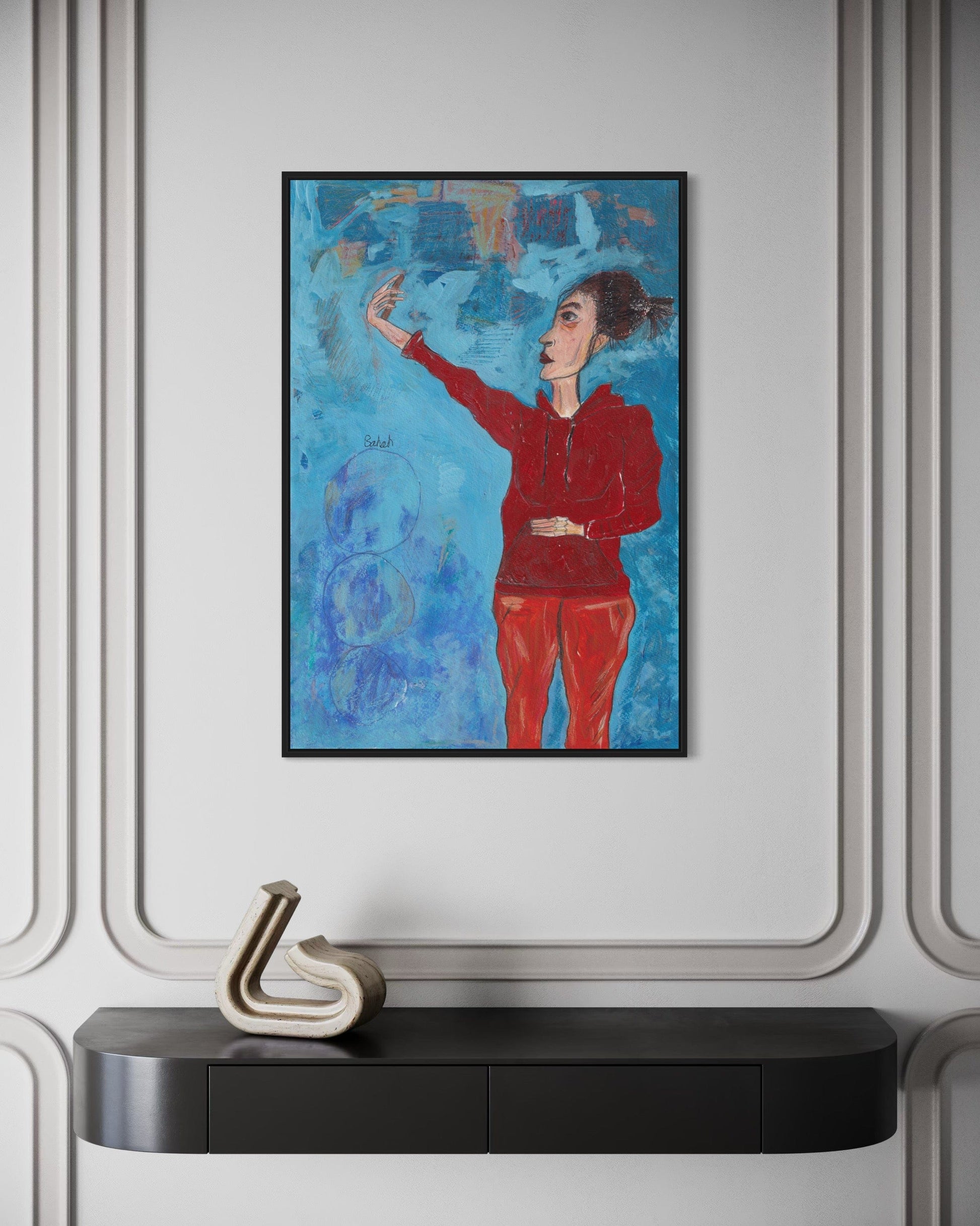 Framed abstract artwork of a person in red against a blue background, displayed on a wall above a black console table.