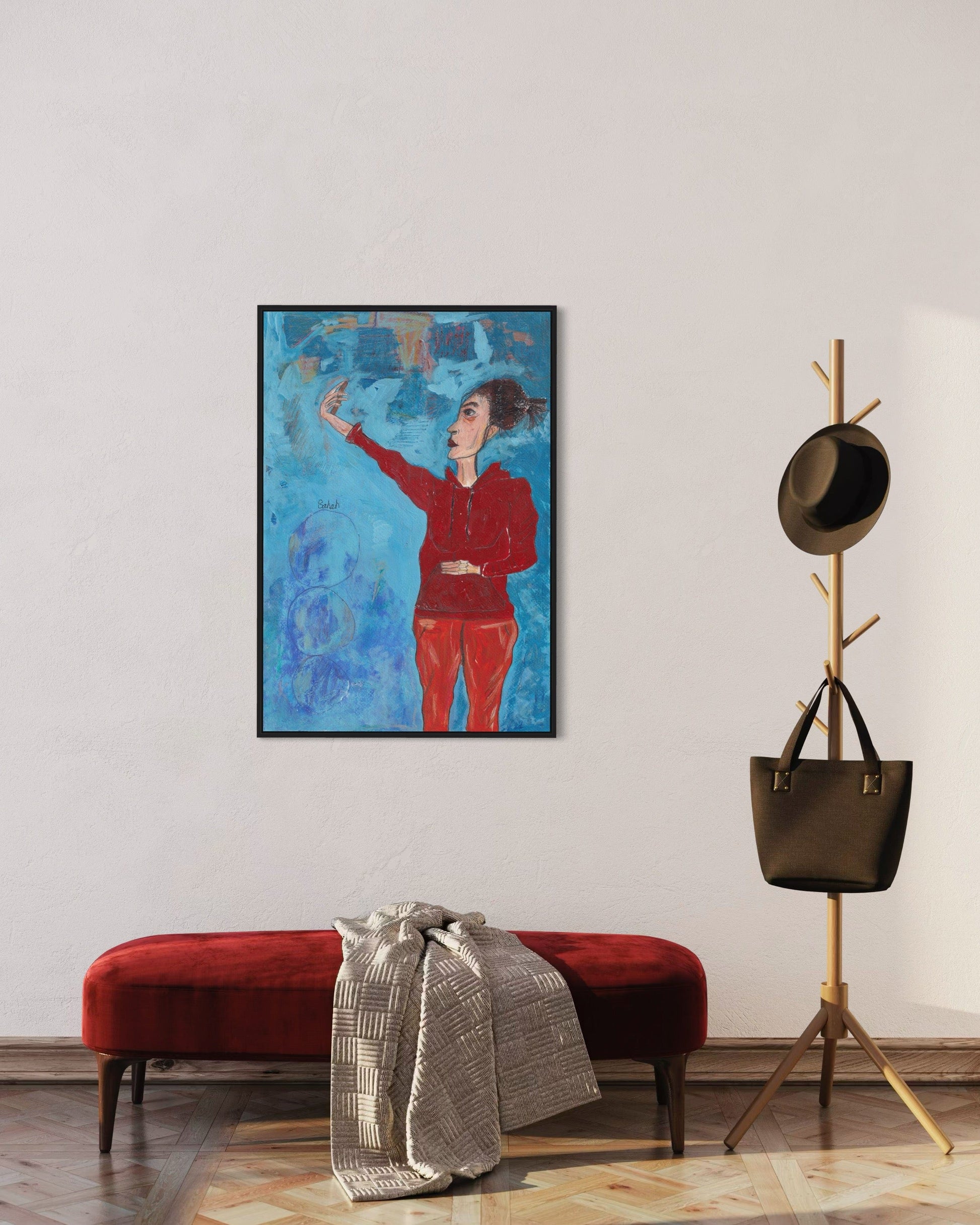 Framed artwork of a person in a red outfit on a wall above a red bench with a coat draped over it, next to a coat rack with a black bag.