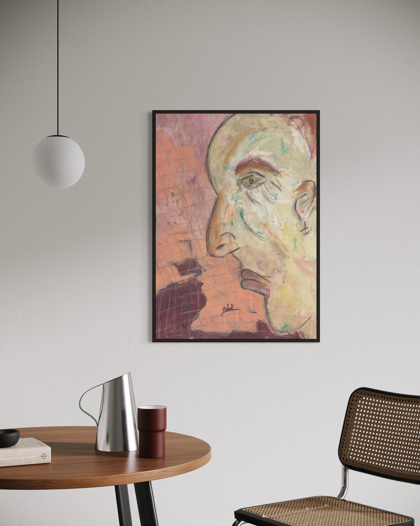 Framed abstract art on a wall above a table with a chair and lamp.