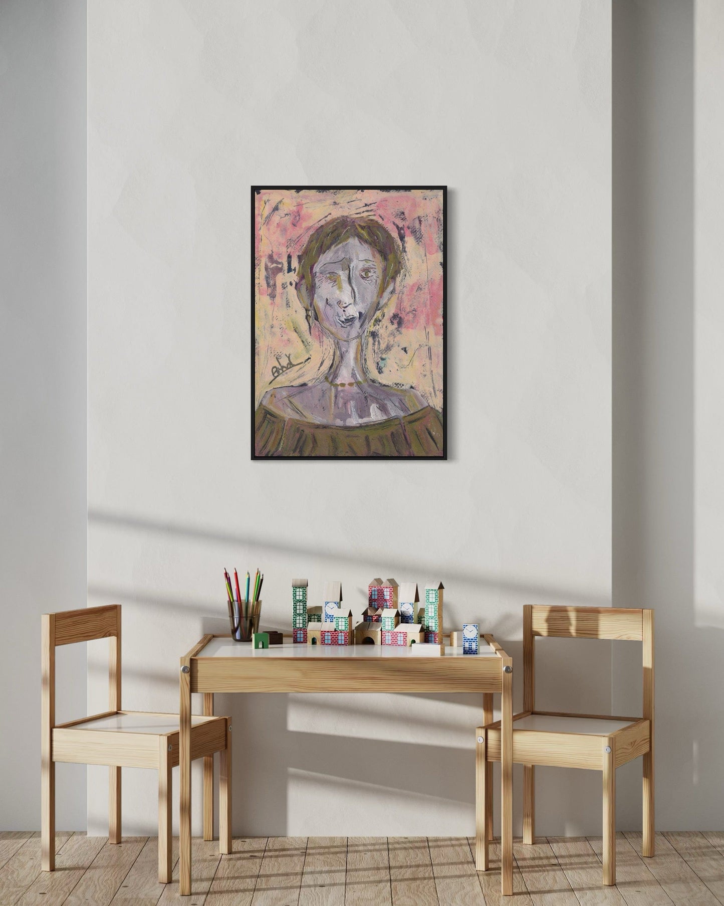 Children's play area with a small wooden table and chairs, art supplies, and a framed painting on the wall.