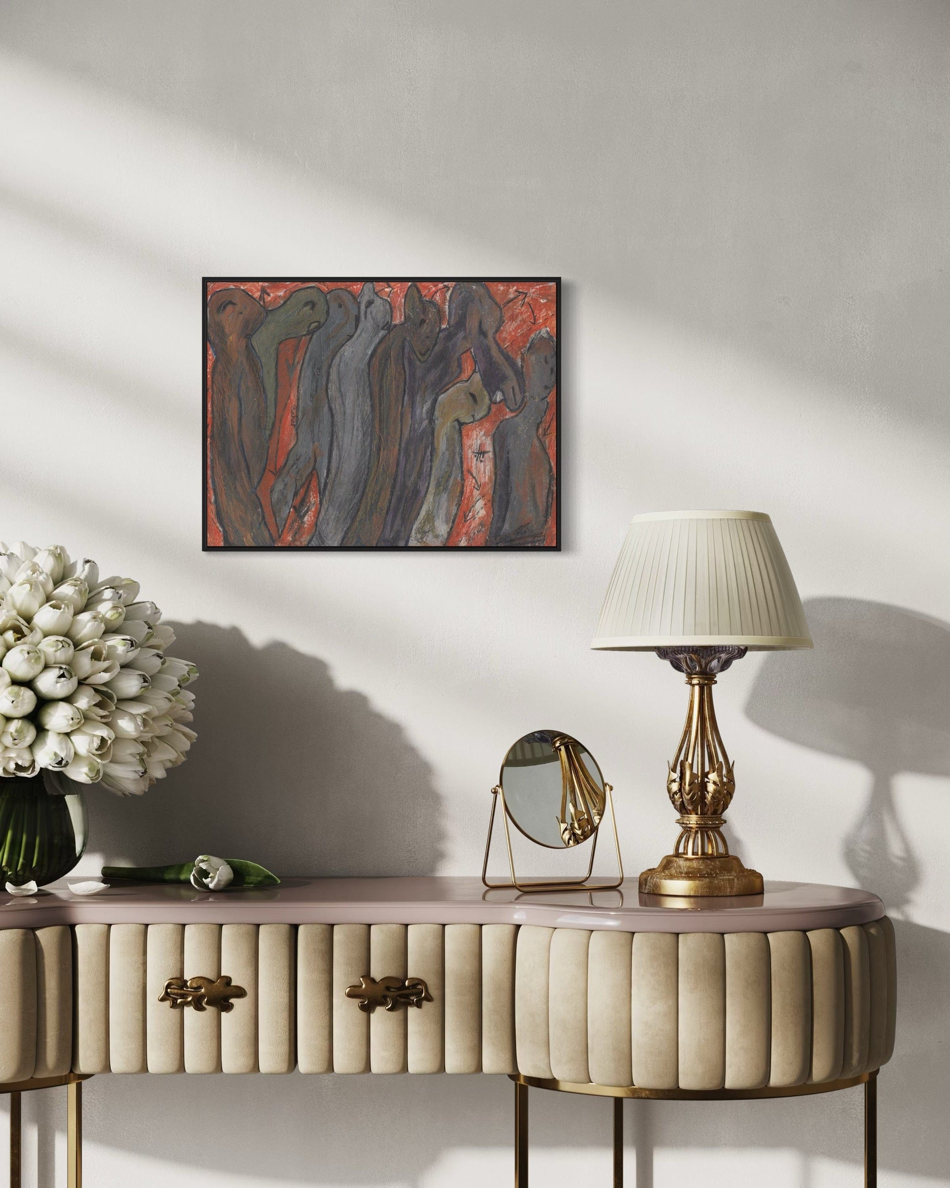 Decorative console table with a lamp, mirror, and flowers against a wall with a framed abstract painting.