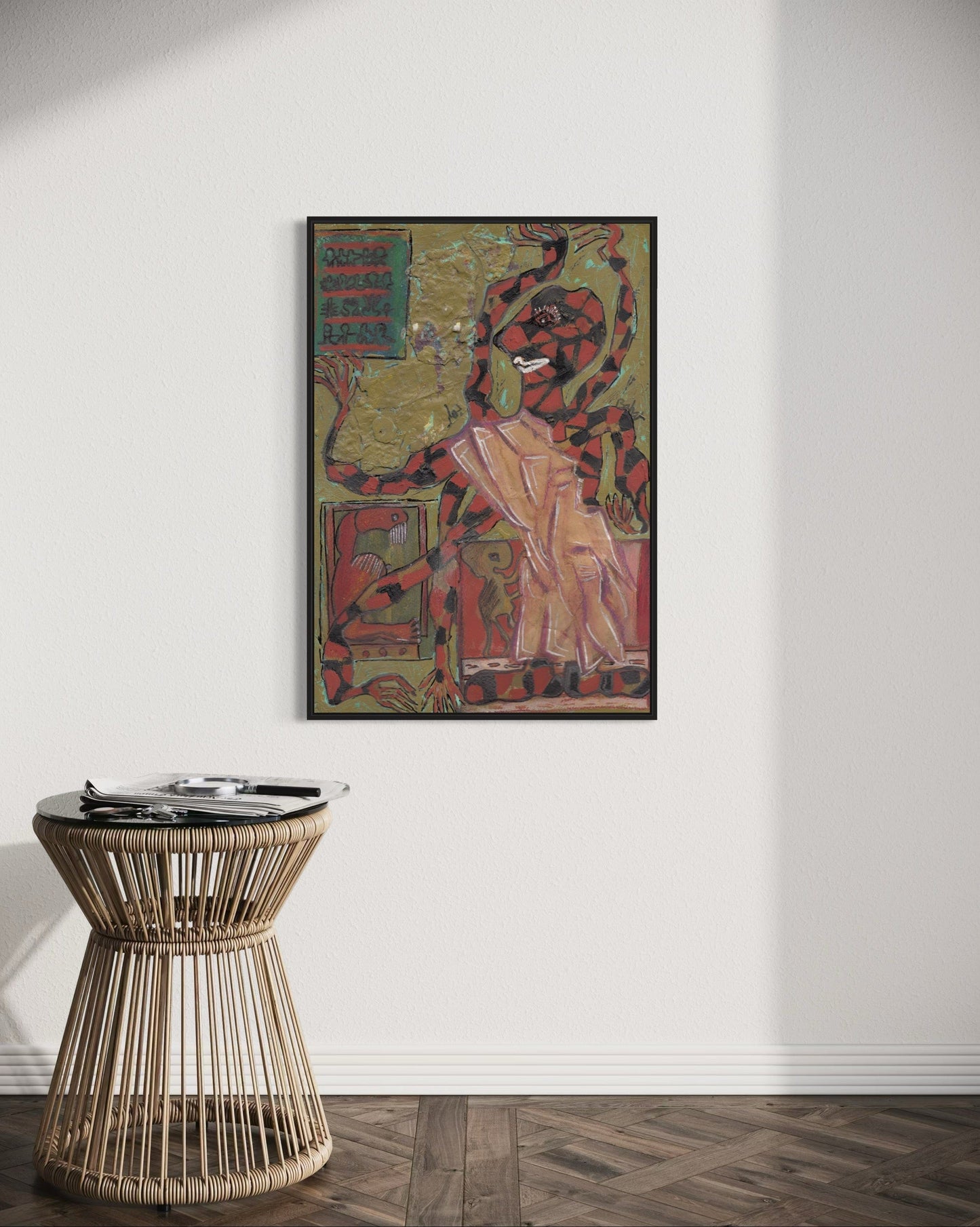 Framed artwork on a wall above a wicker side table in a room.