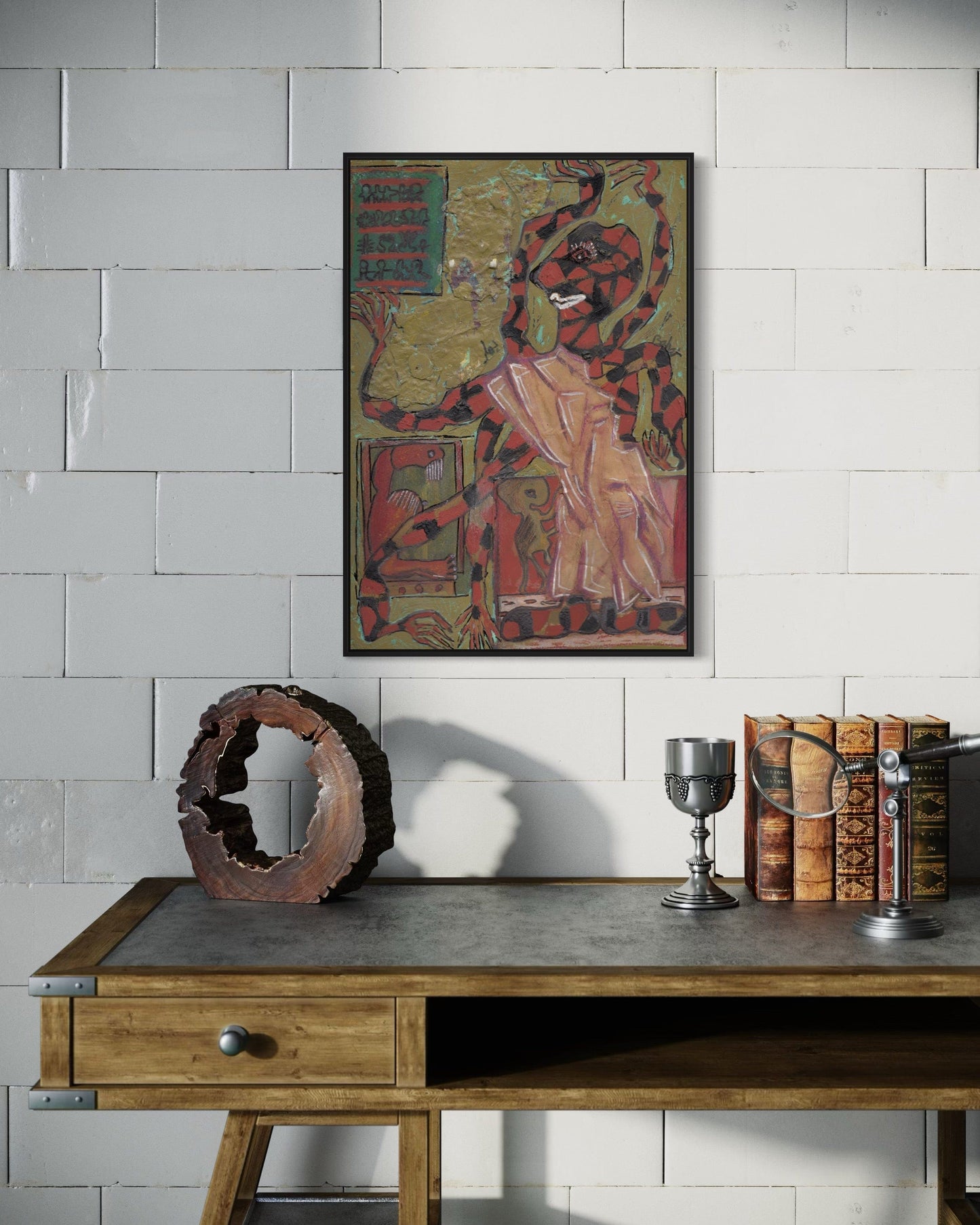Decorative setup with a framed artwork, books, and a metal container on a wooden table against a tiled wall.
