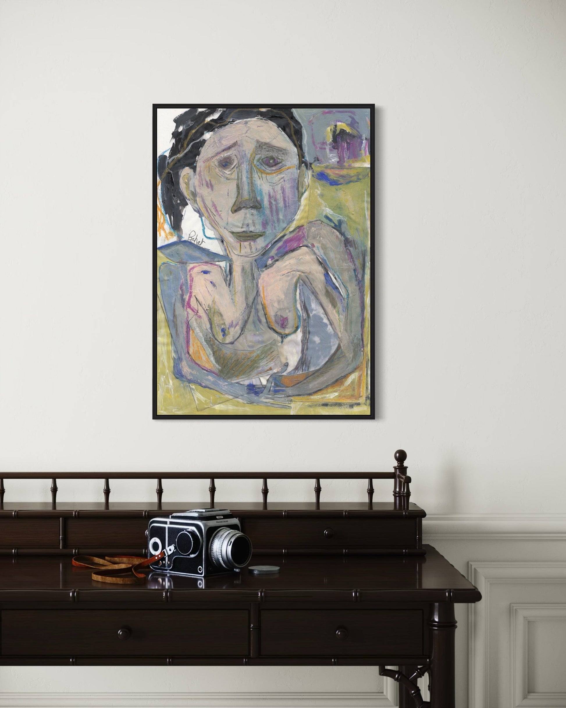 Framed painting of a nude figure on a wall above a dark wooden desk with an old camera.