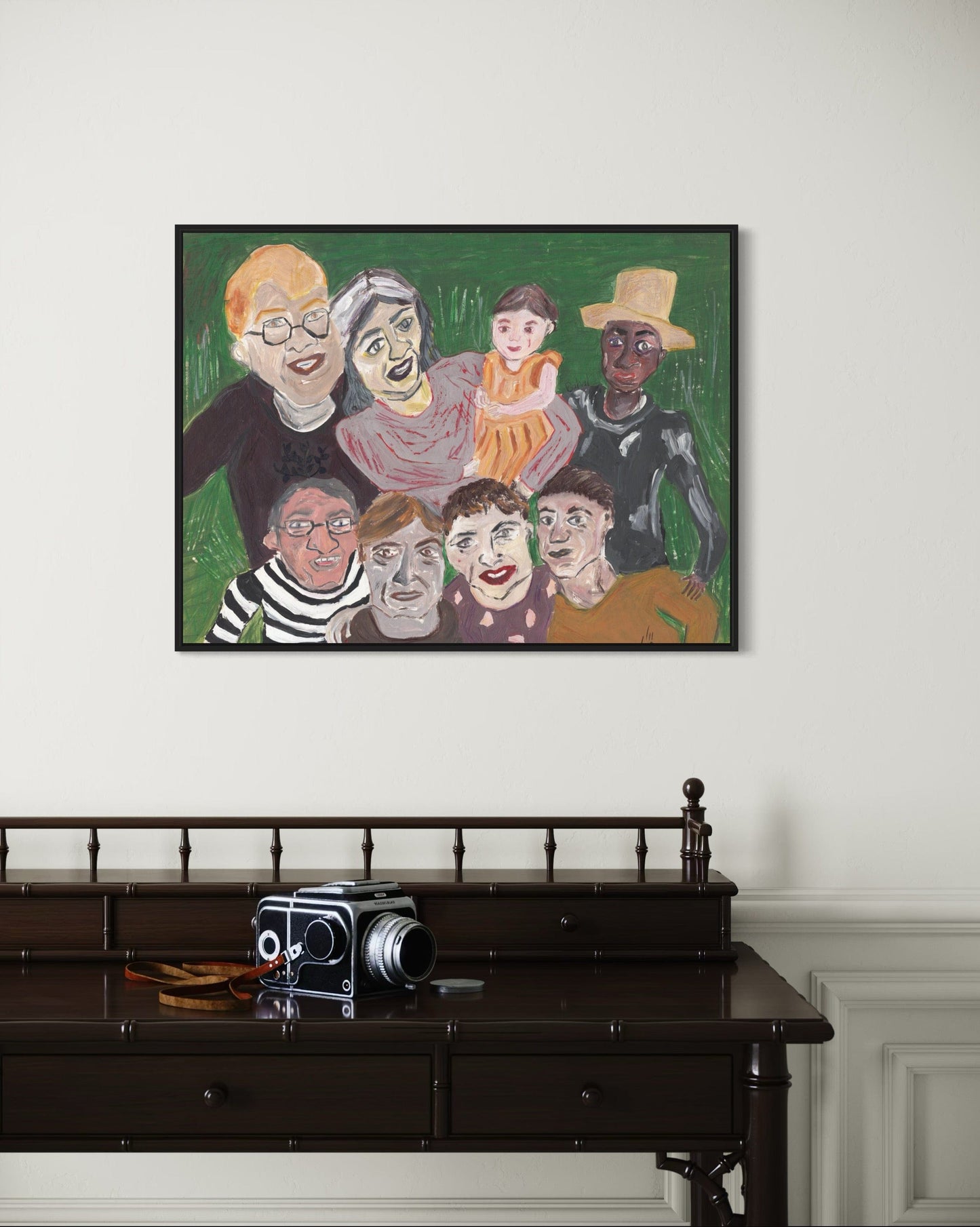 Framed artwork of a diverse group of people on a wall above a wooden desk with an old camera.