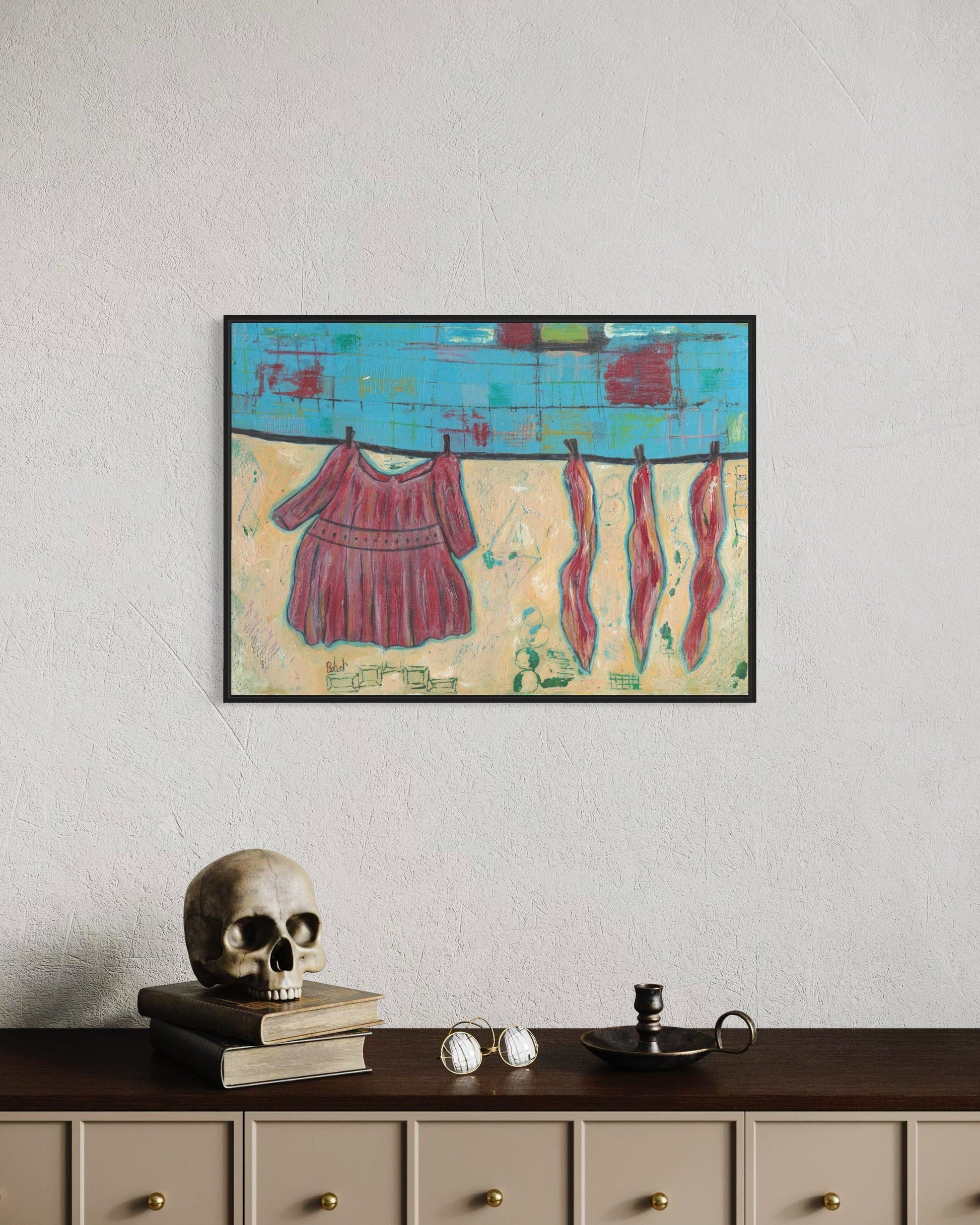 Framed abstract painting of clothes on a line above a shelf with decorative items.