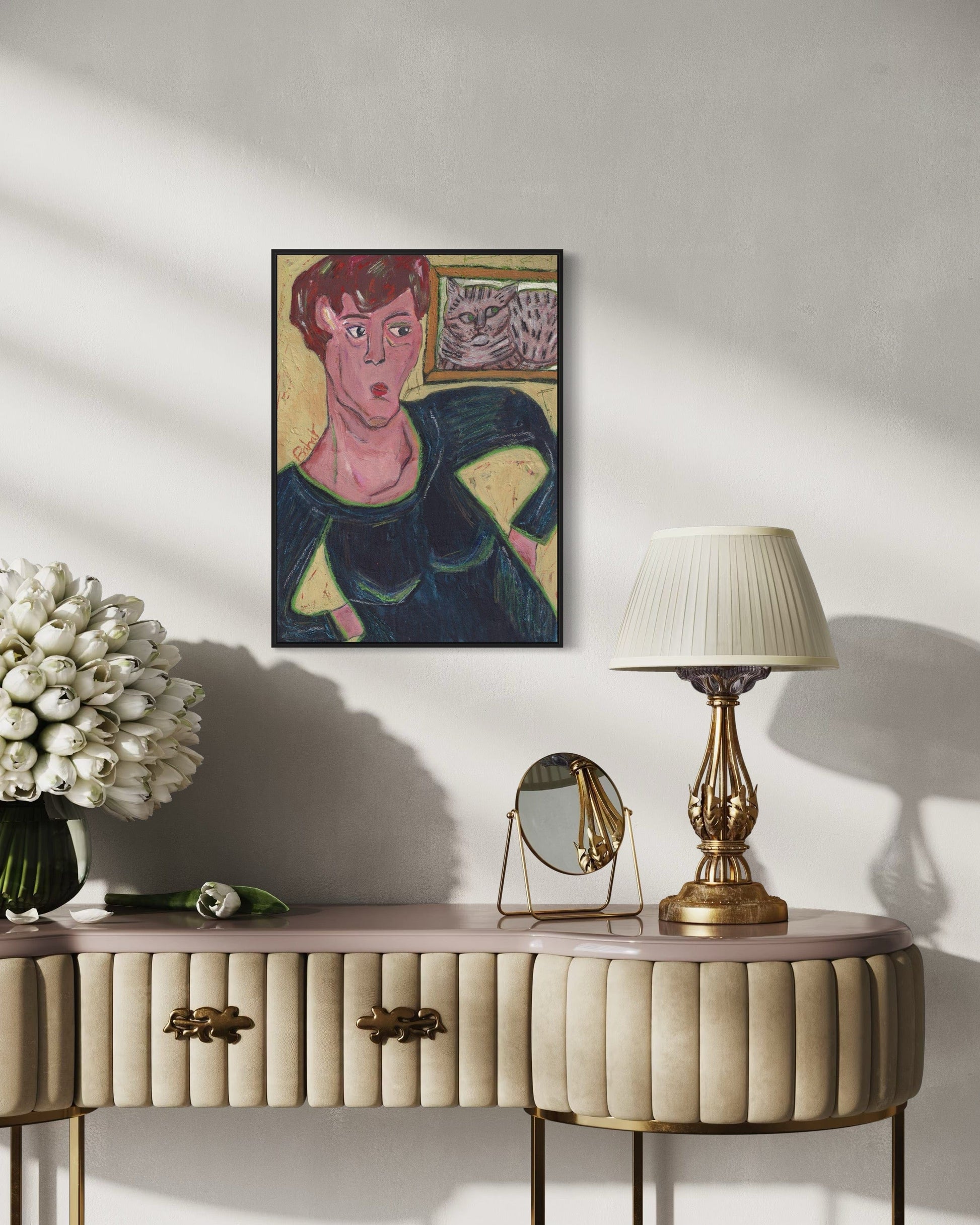 Decorative console table with a lamp, mirror, and flowers against a wall with a framed painting.