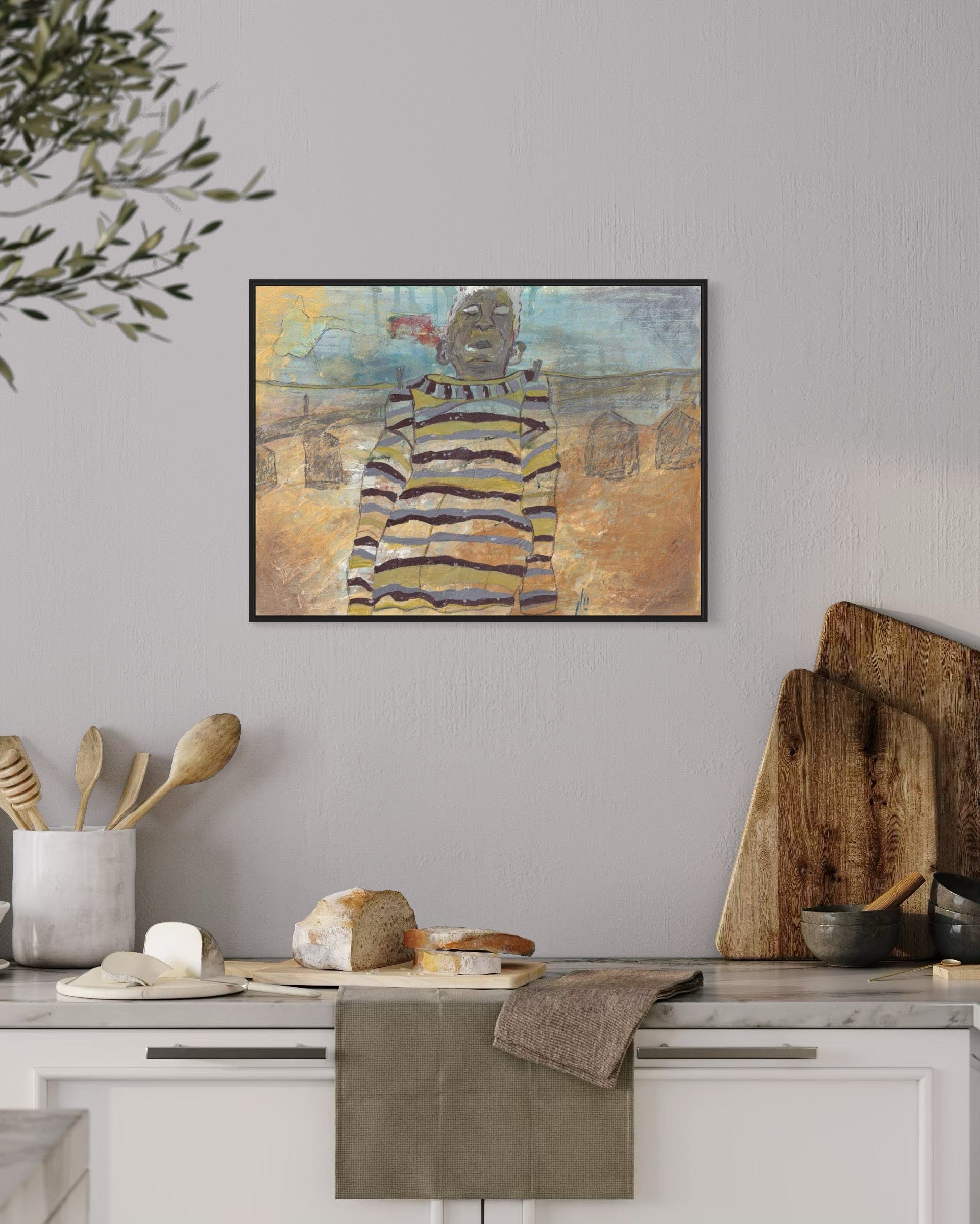 Framed abstract art piece on a wall above a kitchen counter with wooden cutting boards and kitchen utensils.