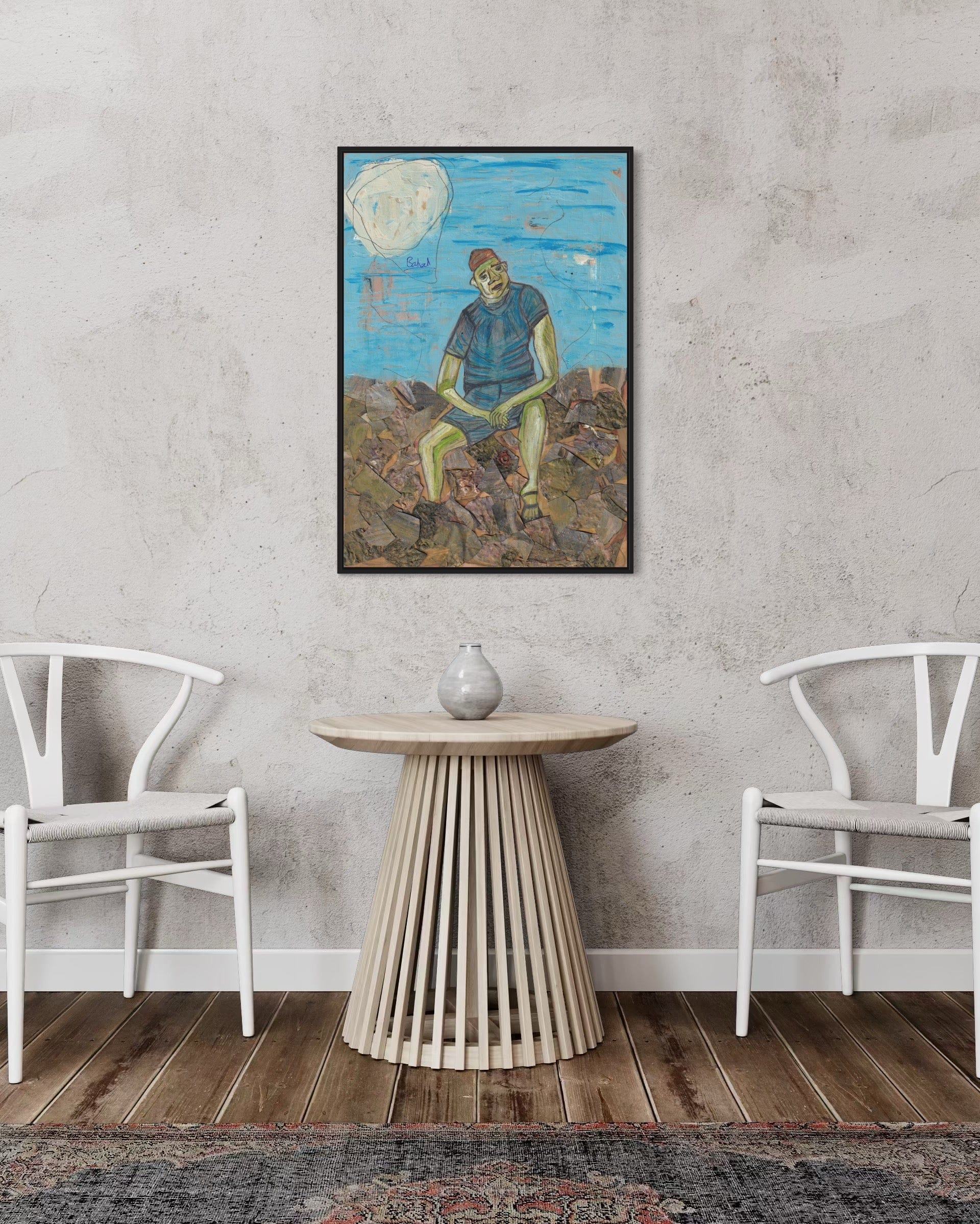 Framed artwork of a person sitting on a rock with a blue sky and clouds, displayed in a room with white chairs and a wooden table.