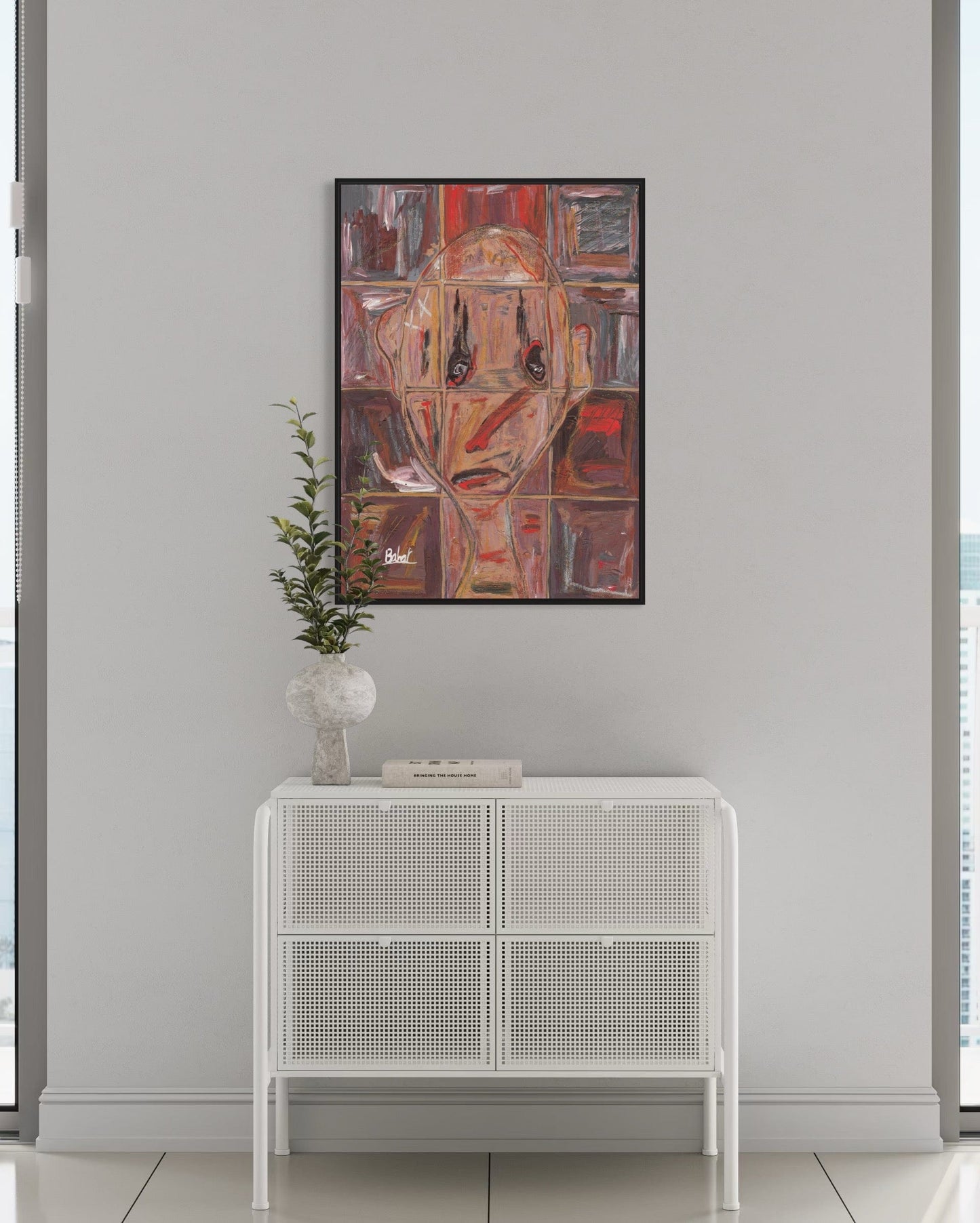 Abstract art piece on a wall above a white cabinet with a plant.