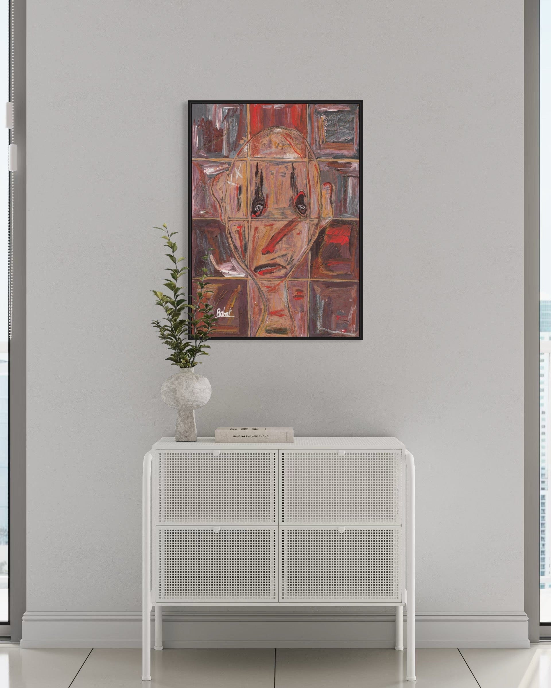 Abstract art piece on a wall above a white cabinet with a plant.