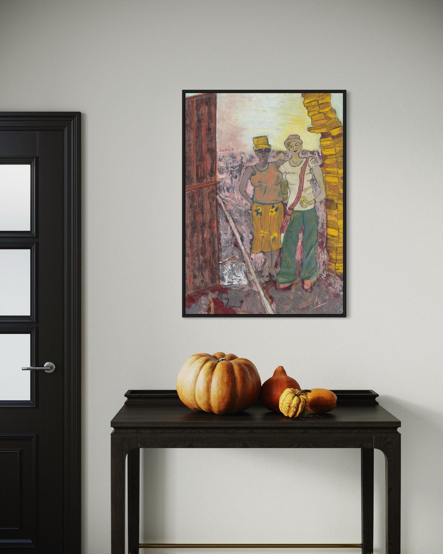 Framed artwork on a wall above a dark wooden table with pumpkins.