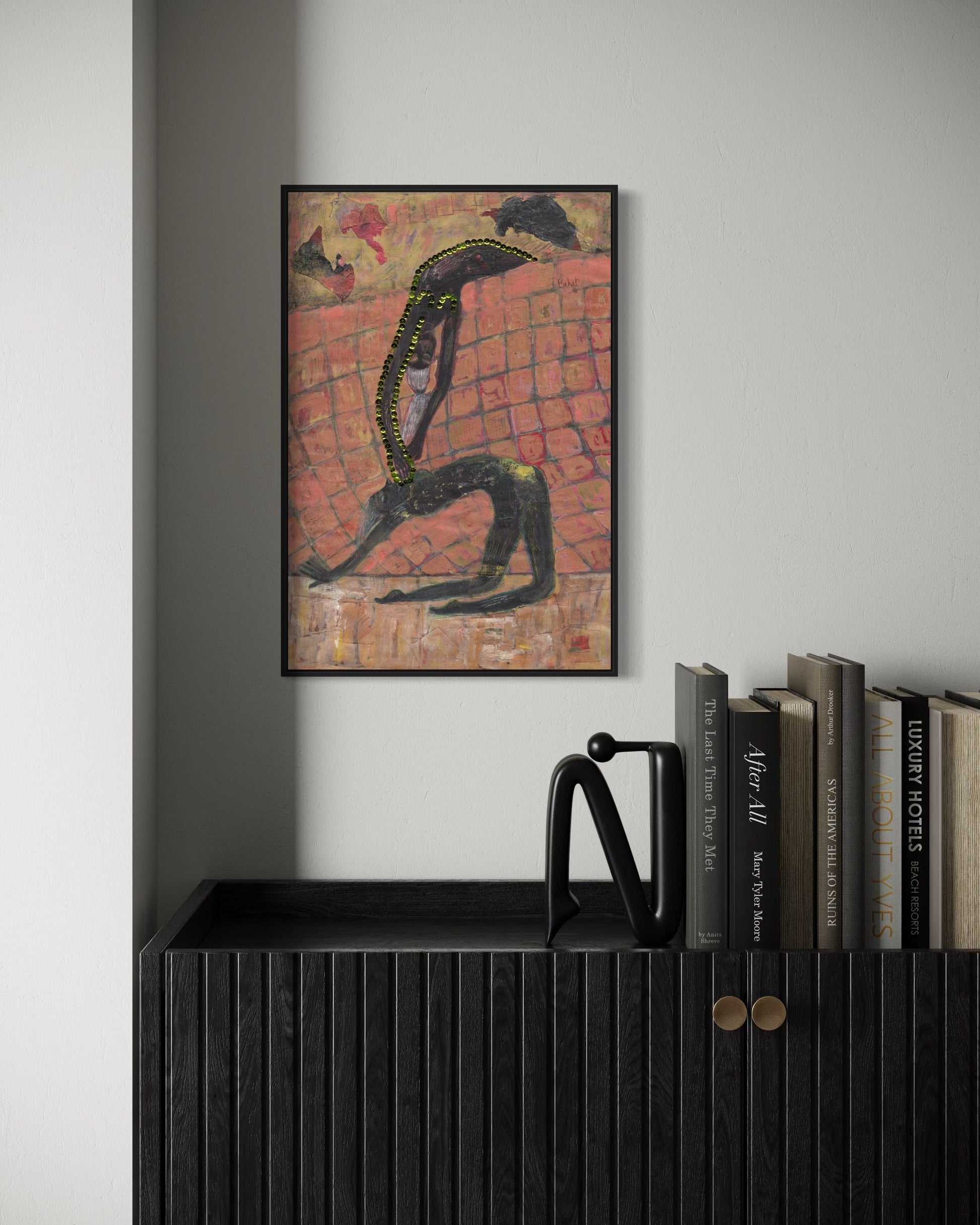 Framed abstract artwork on a wall above a black cabinet with books.