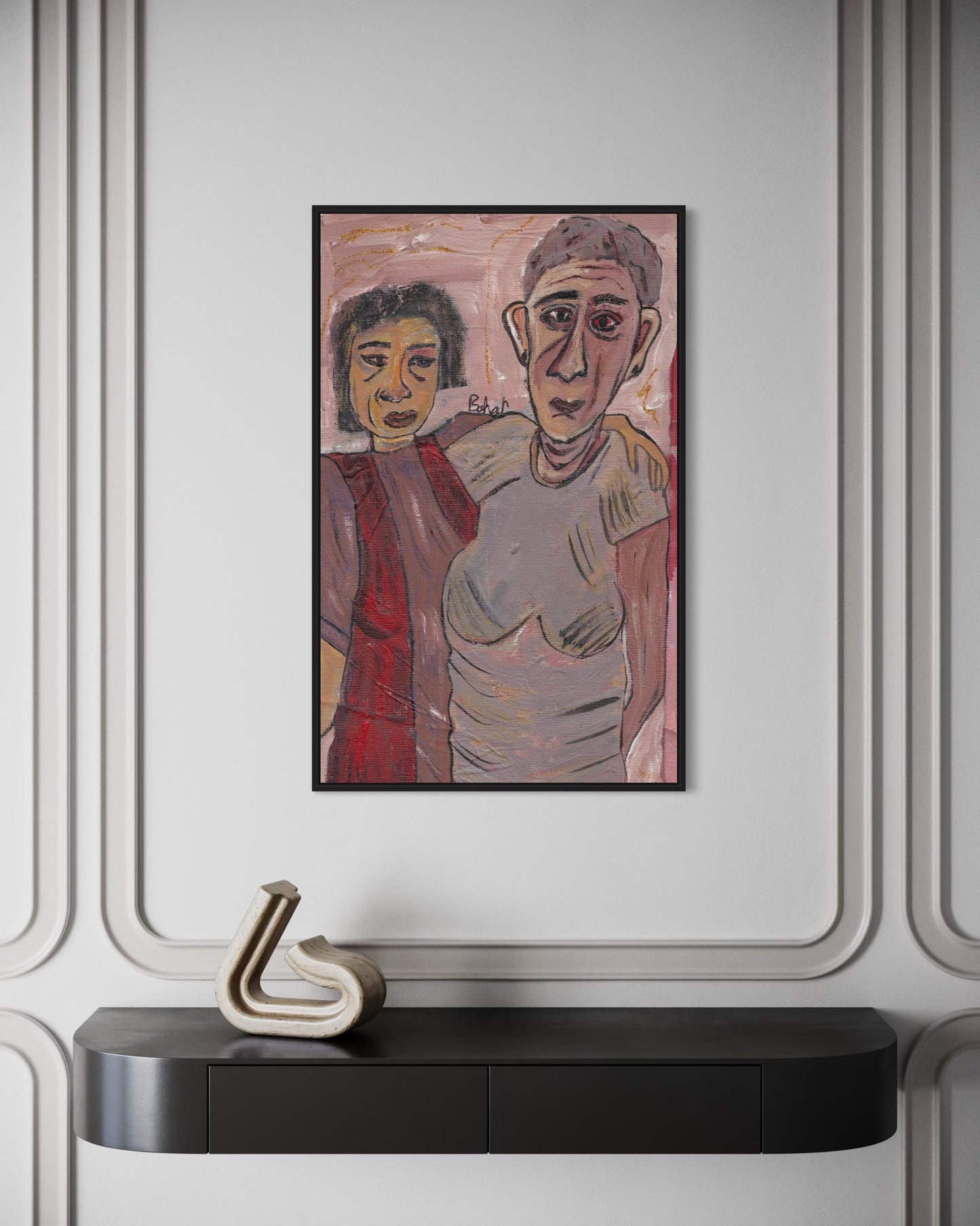 Framed artwork of two people on a wall above a black console table with a decorative object.