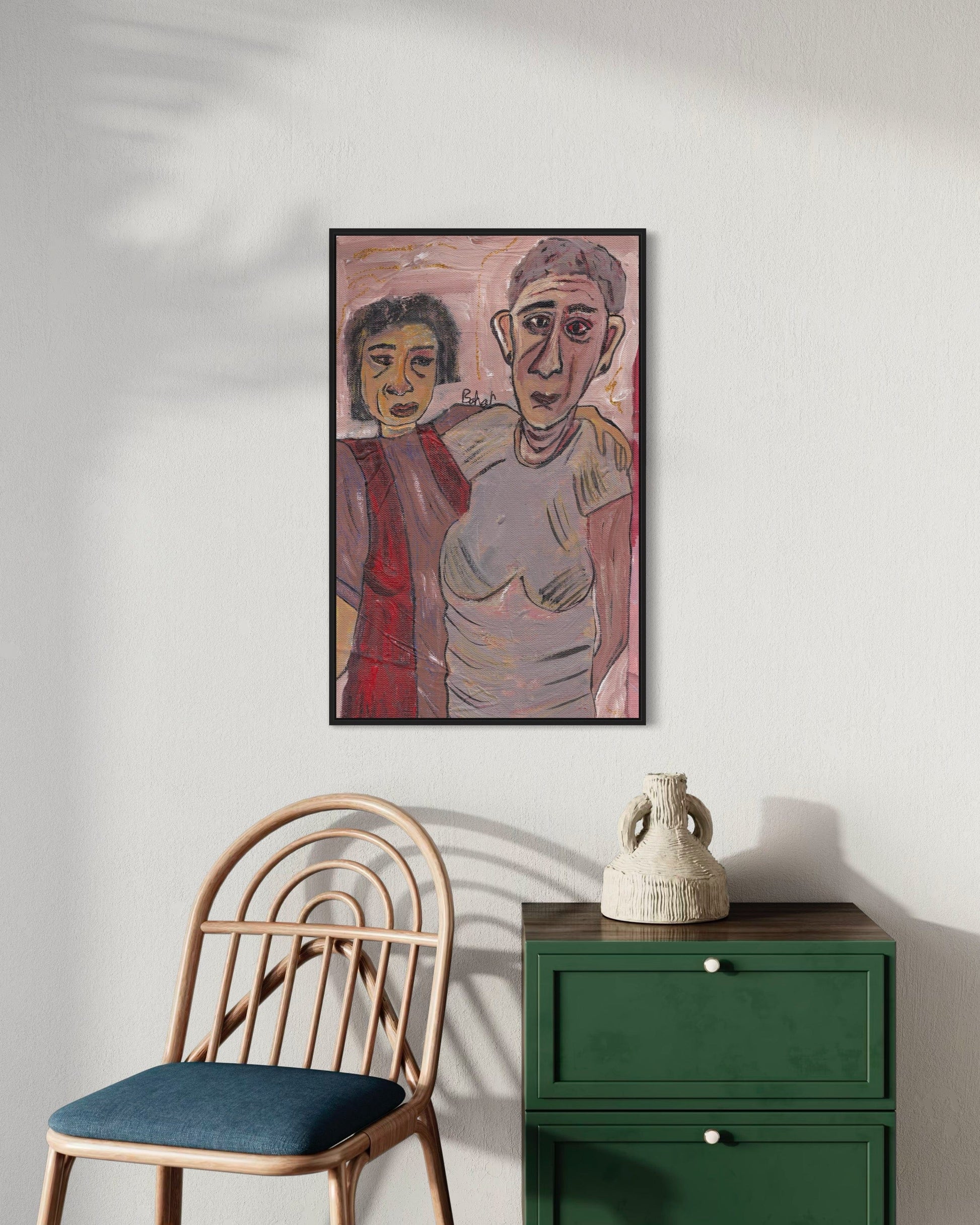 Framed artwork of two people on a wall above a chair and green cabinet.