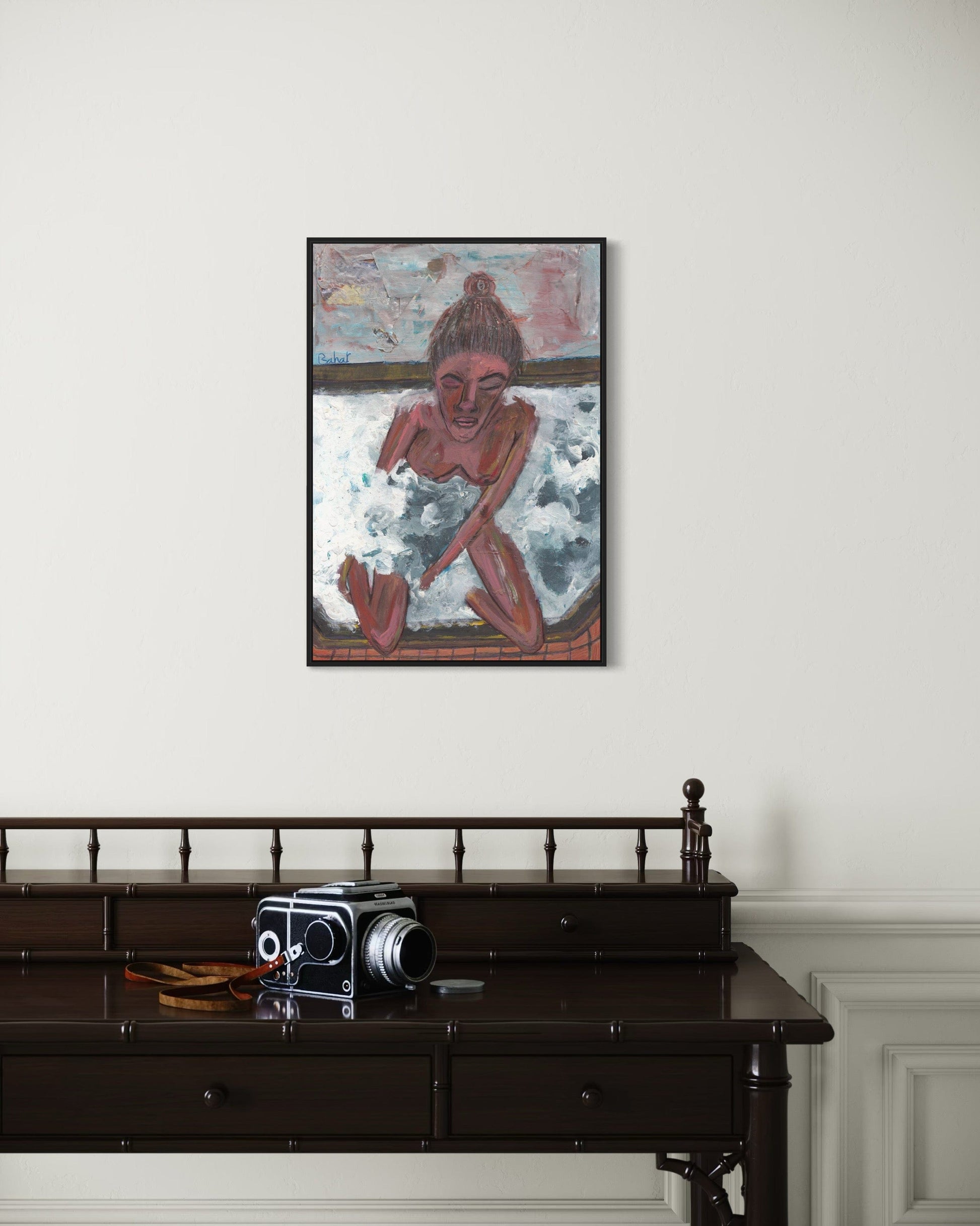 Framed artwork of a person with a surfboard on a white wall above a dark wooden desk with an old camera.