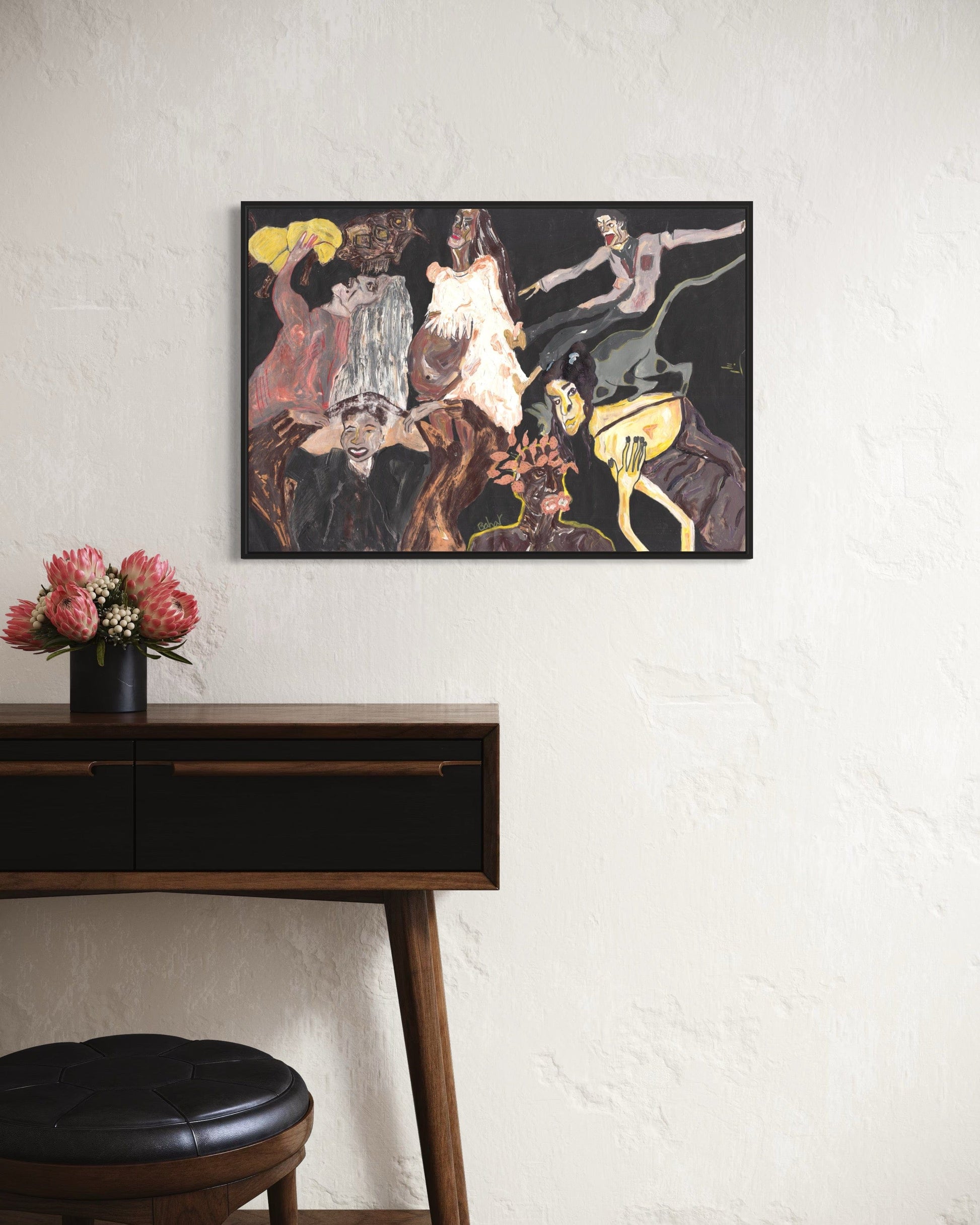 Framed abstract artwork on a wall above a wooden desk with flowers.