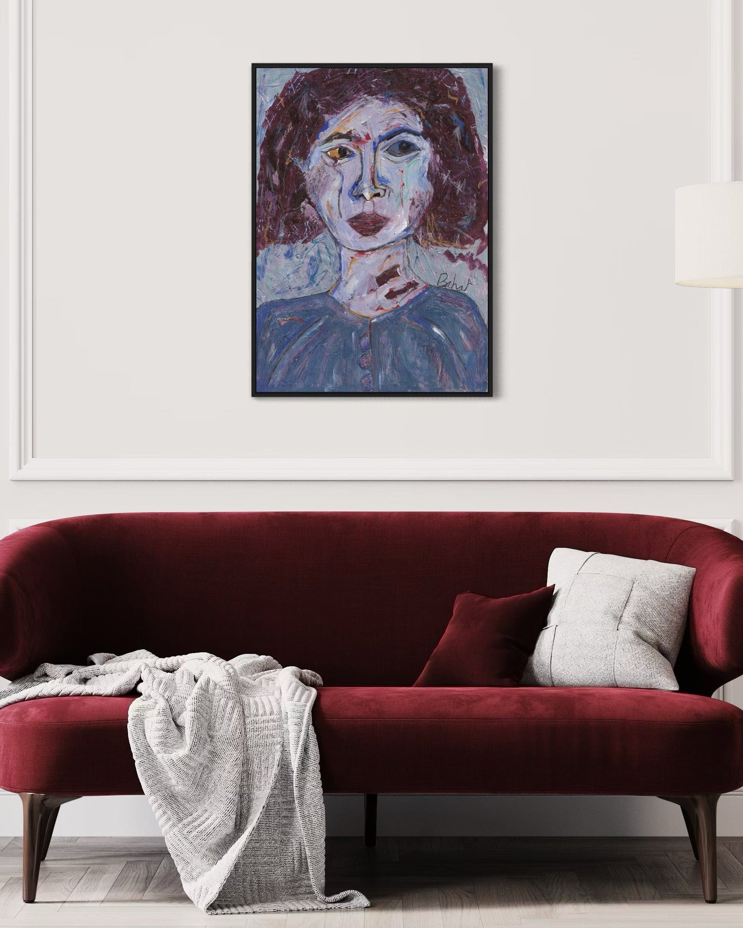 Red sofa with a white blanket and gray pillow, framed artwork above on a white wall.