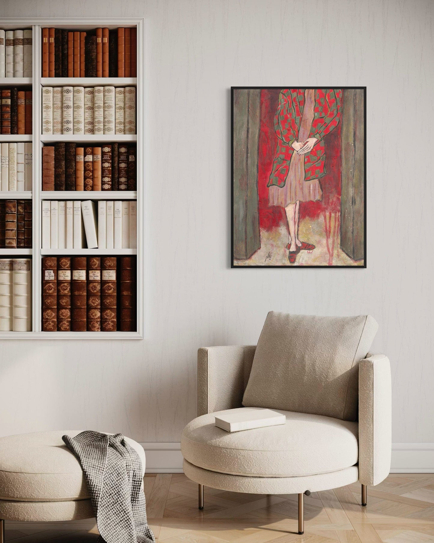 Beige armchair with a pillow in a room with a bookshelf and a framed artwork on the wall.