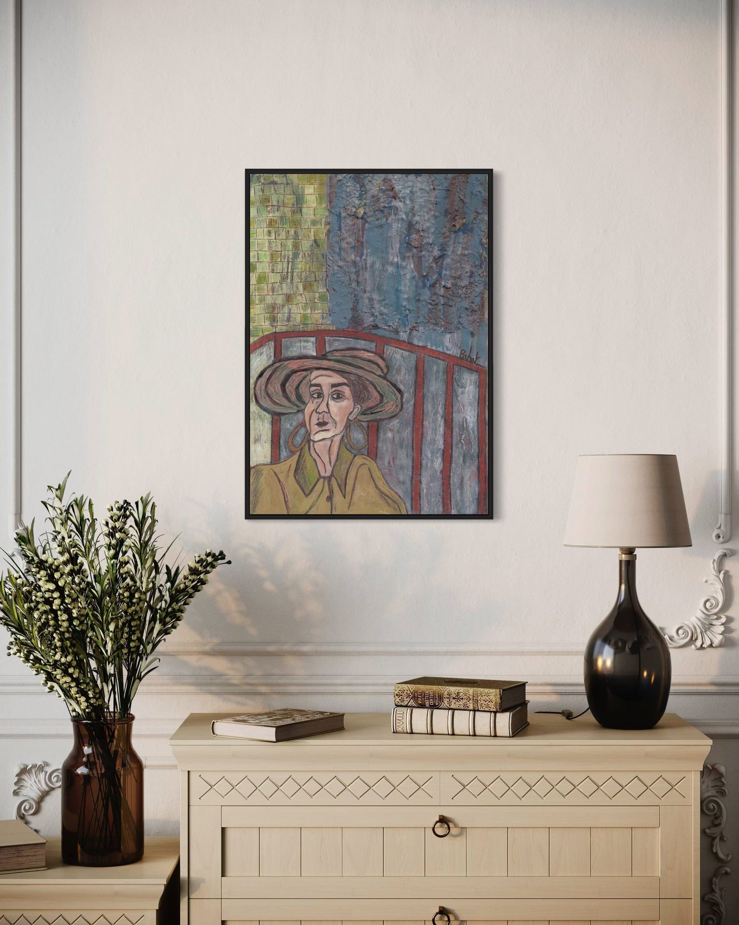 Framed artwork of a person with a hat on a wall above a cabinet with decorative items.