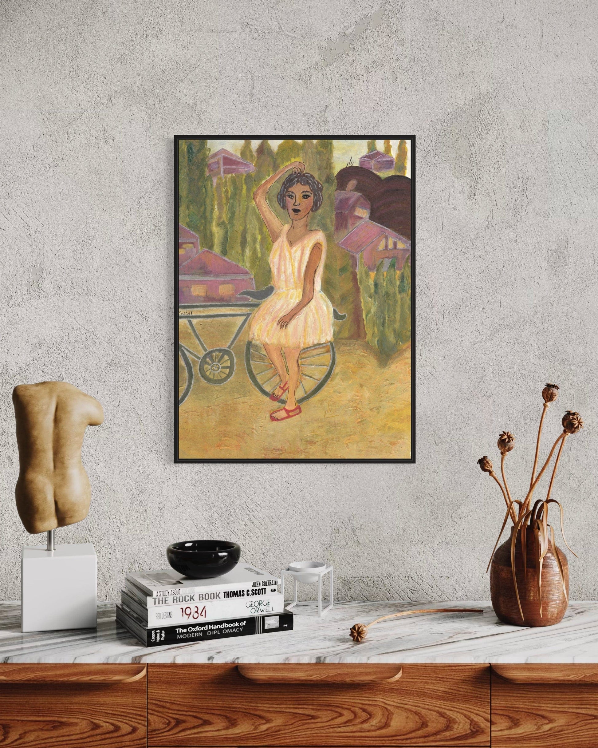 Framed artwork of a woman with a bicycle on a wall above a wooden shelf.