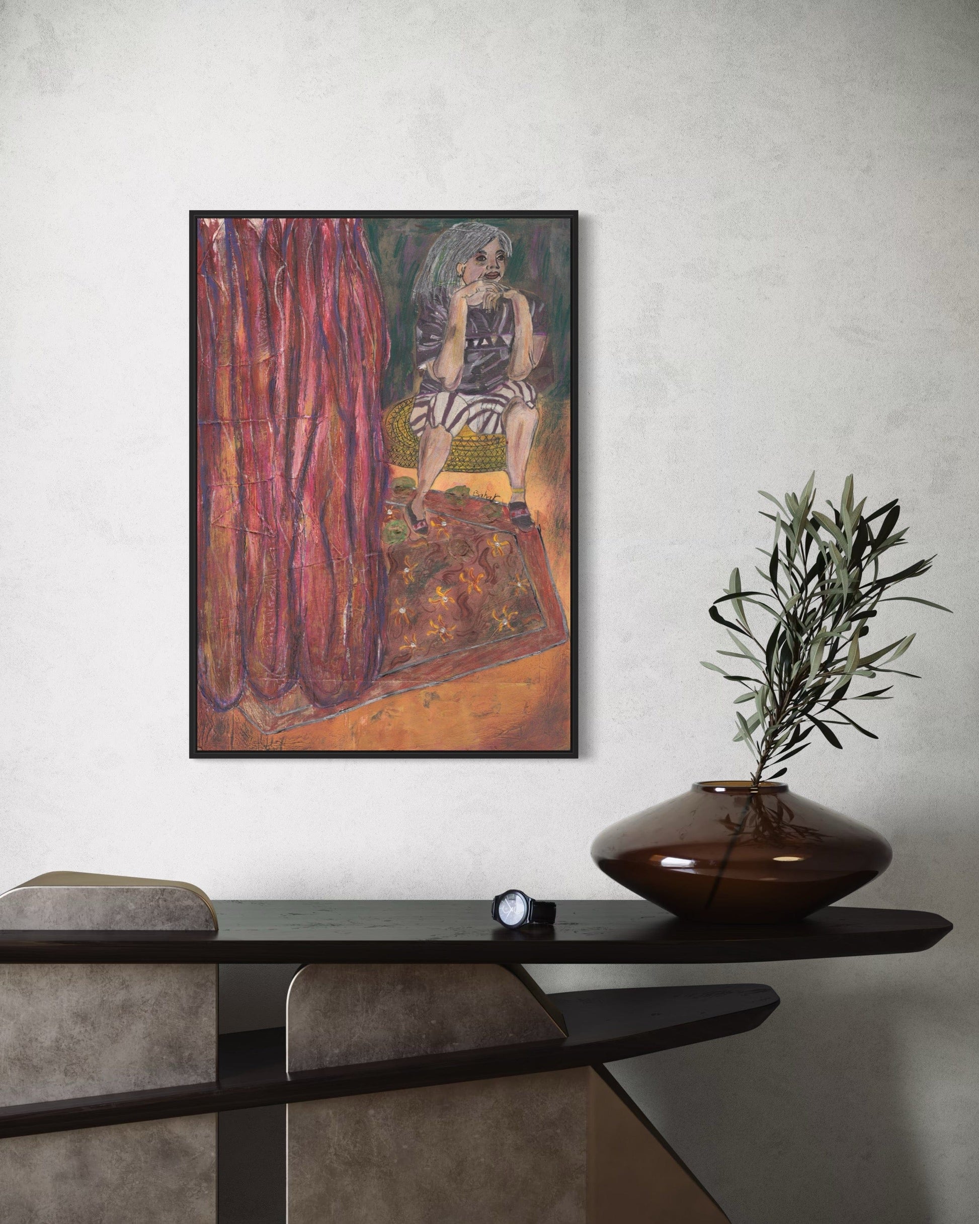 Framed artwork on a wall above a table with a decorative vase and plant.