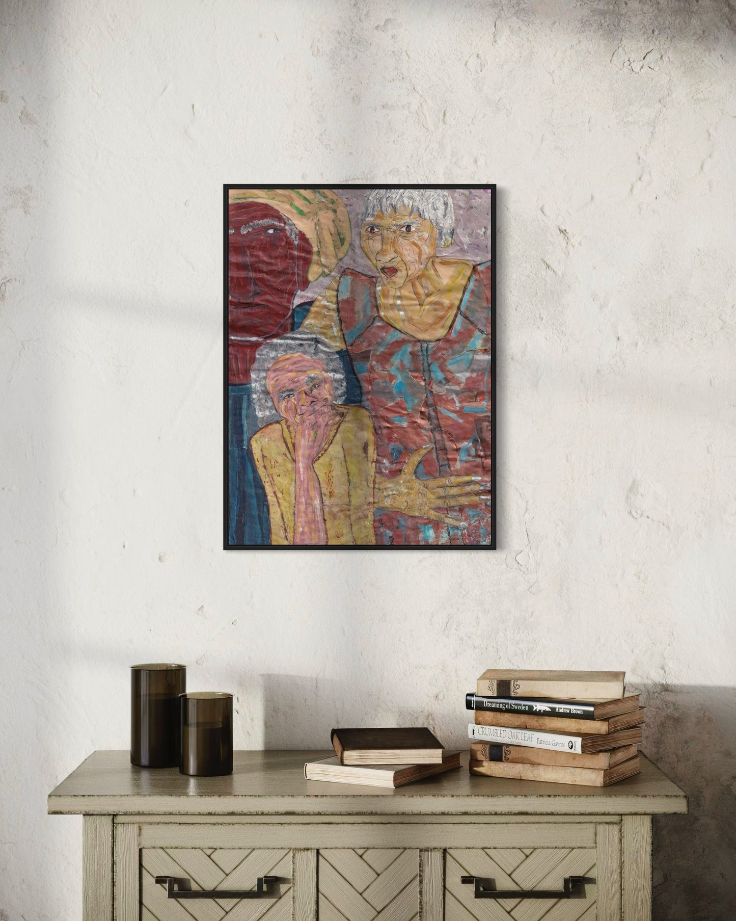 Framed artwork of two figures on a textured wall above a wooden cabinet with books.
