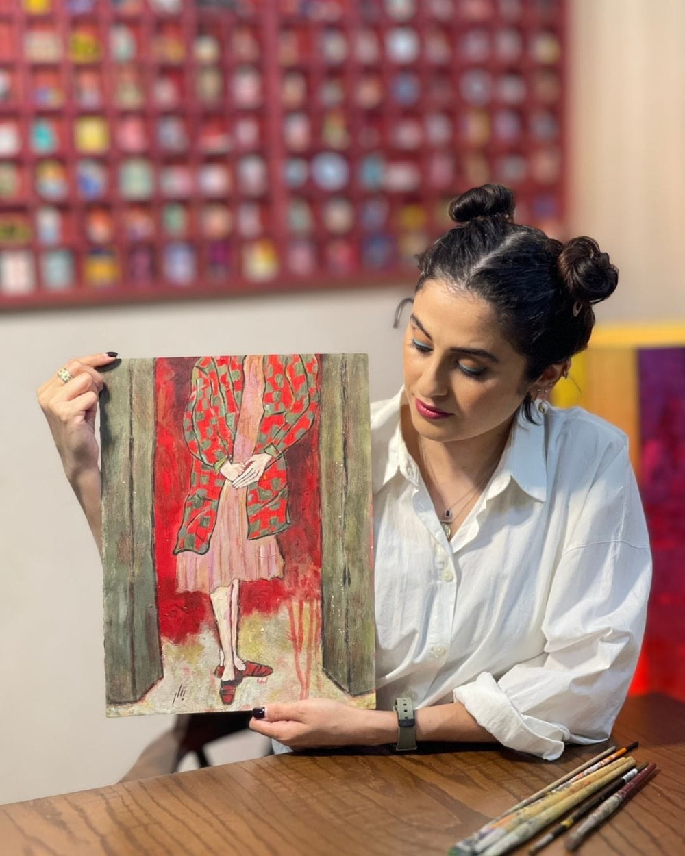 Woman holding a painting of a woman in a red dress in an art studio.