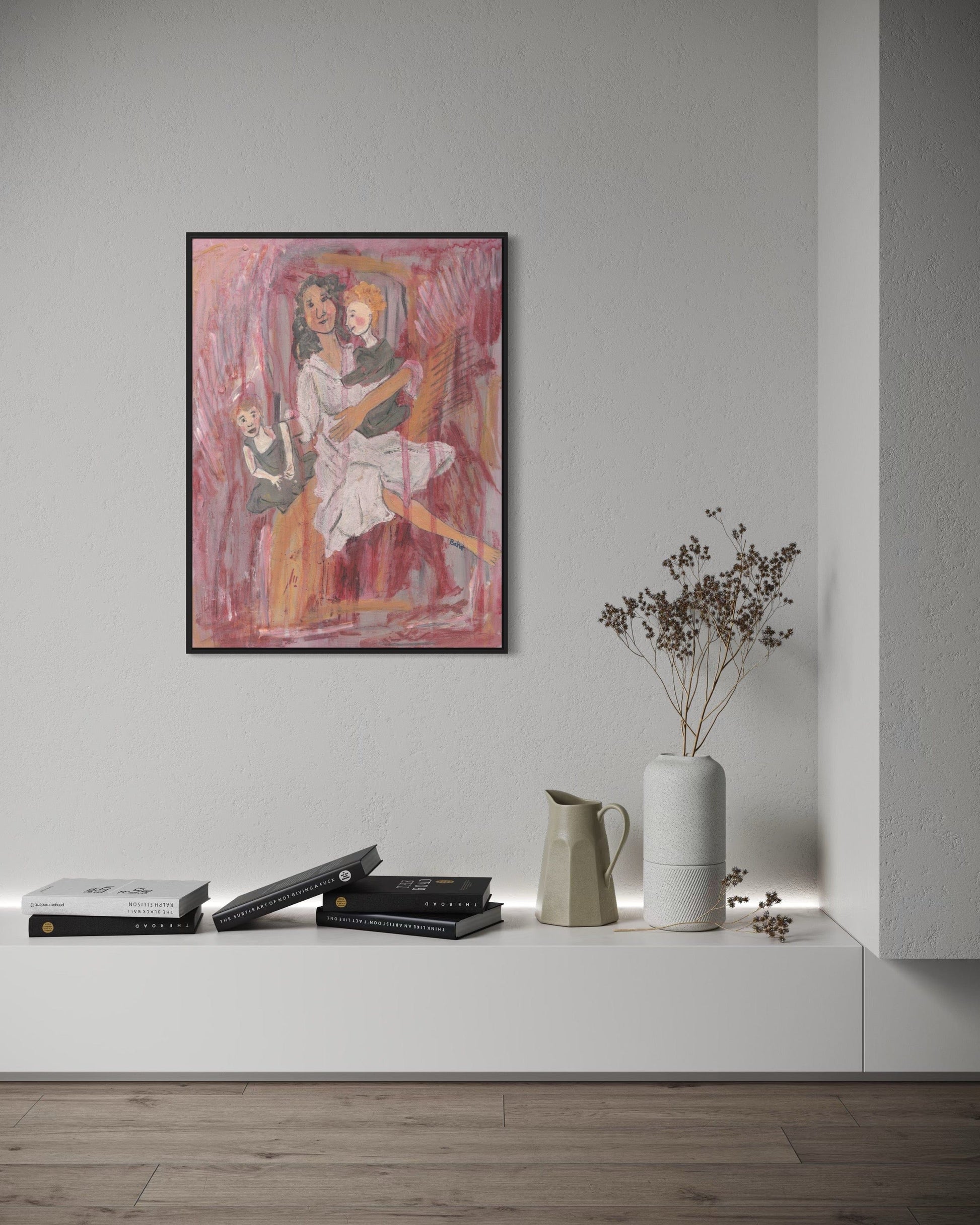 Framed artwork on a wall above a shelf with books and a vase.