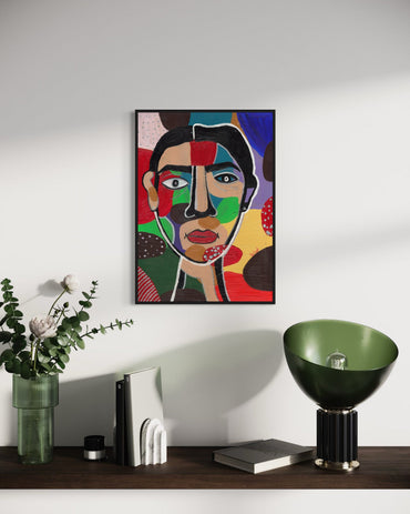 Framed abstract art of a face on a wall above a wooden shelf with decorative items.