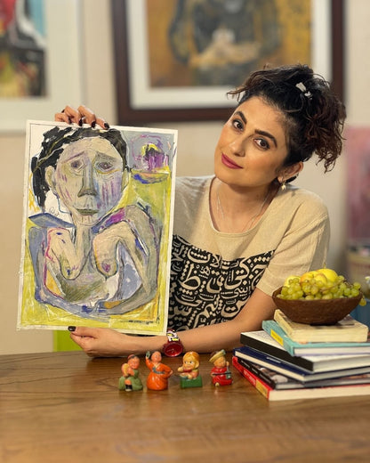 Woman holding a painting of a woman's torso in a room with books and figurines on a table.