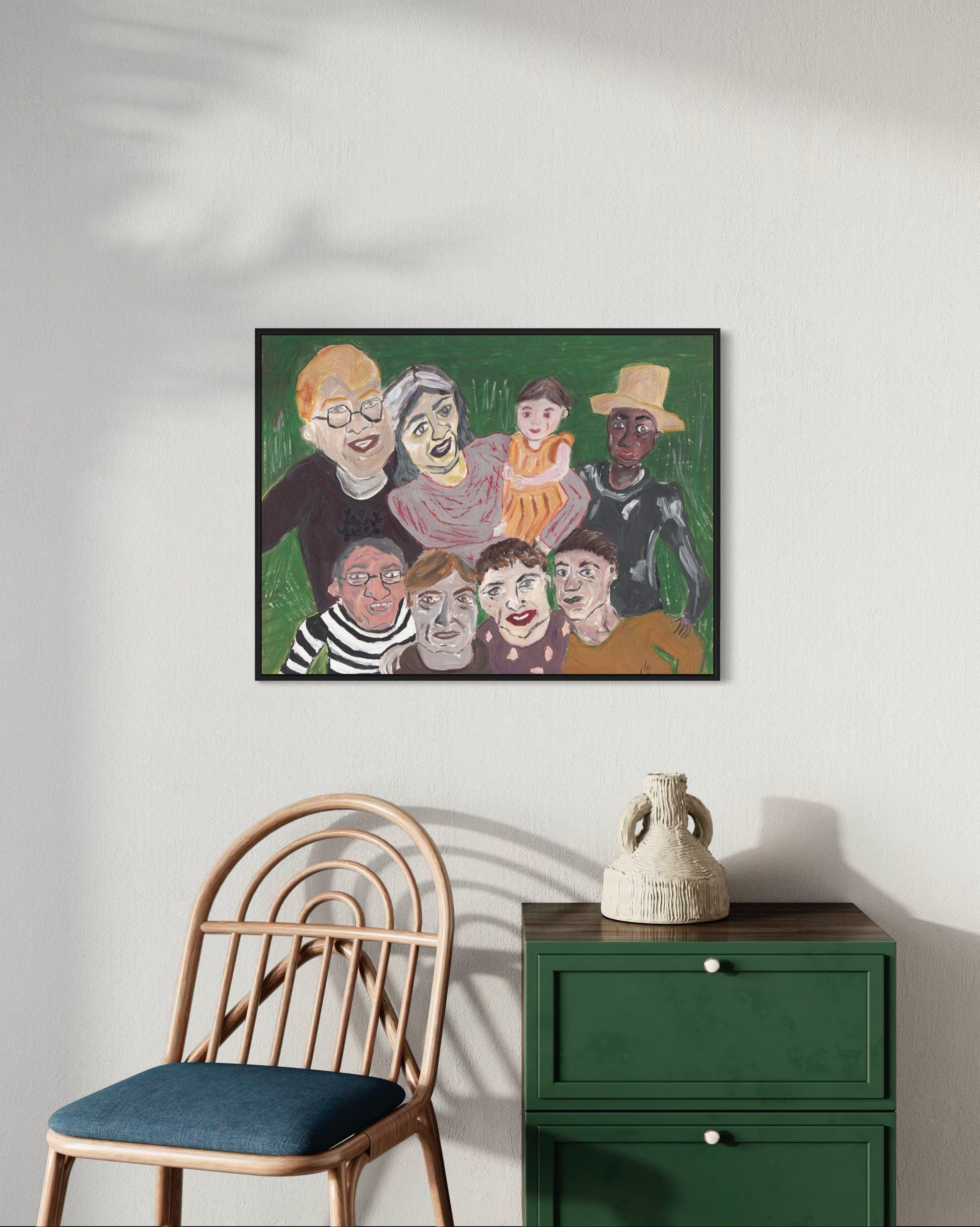 Framed artwork of a diverse group of people on a wall above a green cabinet and chair.