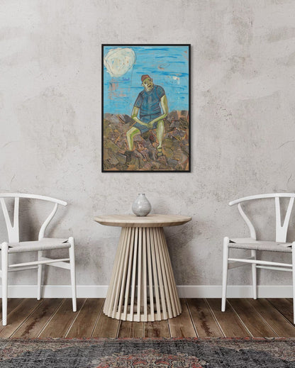 Framed artwork of a person sitting on a rock with a blue sky and clouds, displayed in a room with white chairs and a wooden table.
