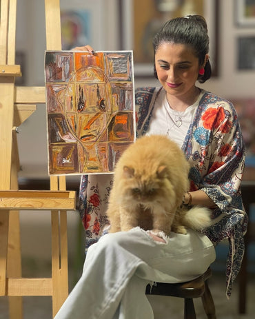 Woman holding a painting with a cat on her lap in an indoor setting