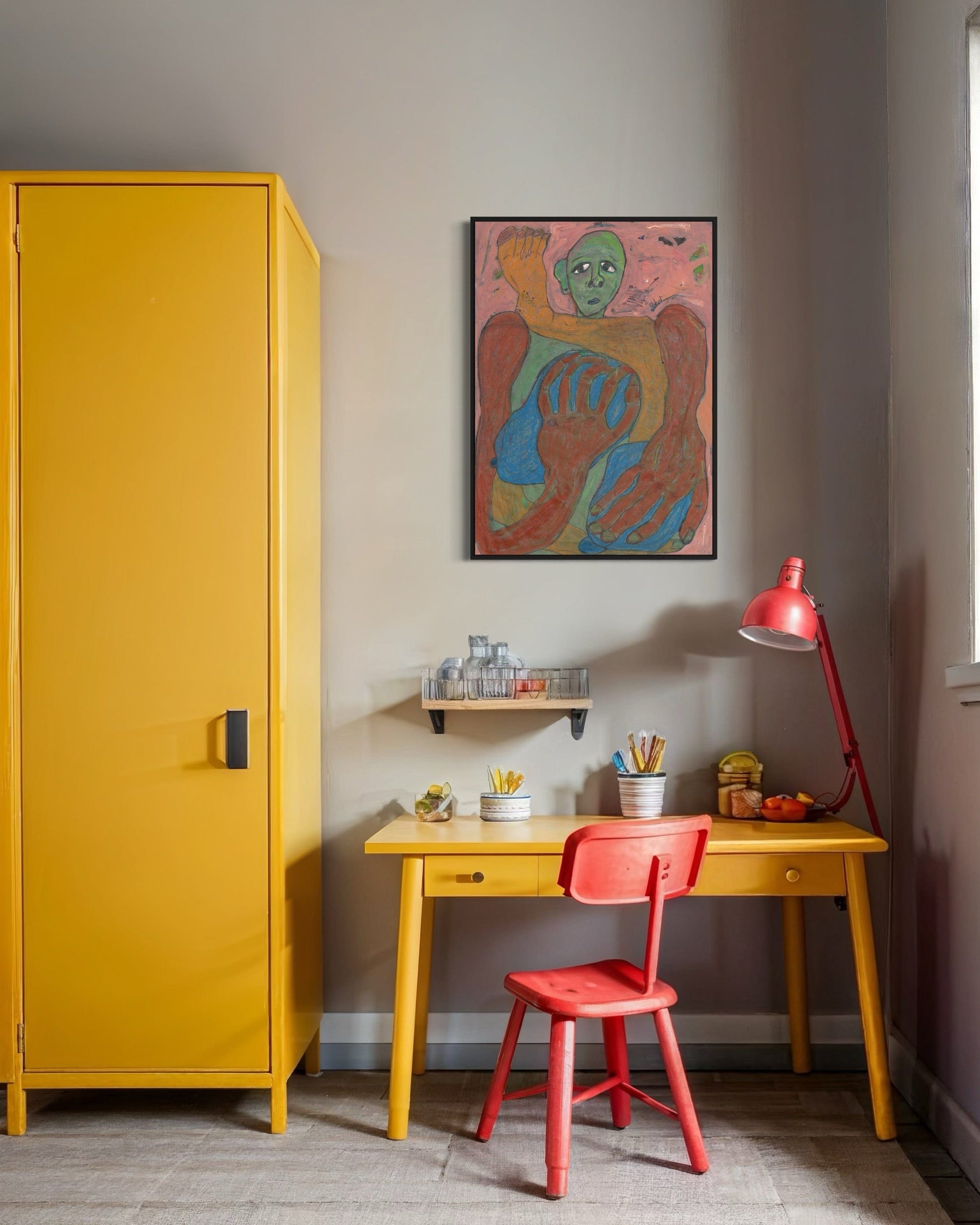 Yellow cabinet, red chair, and desk with colorful artwork on a gray wall.
