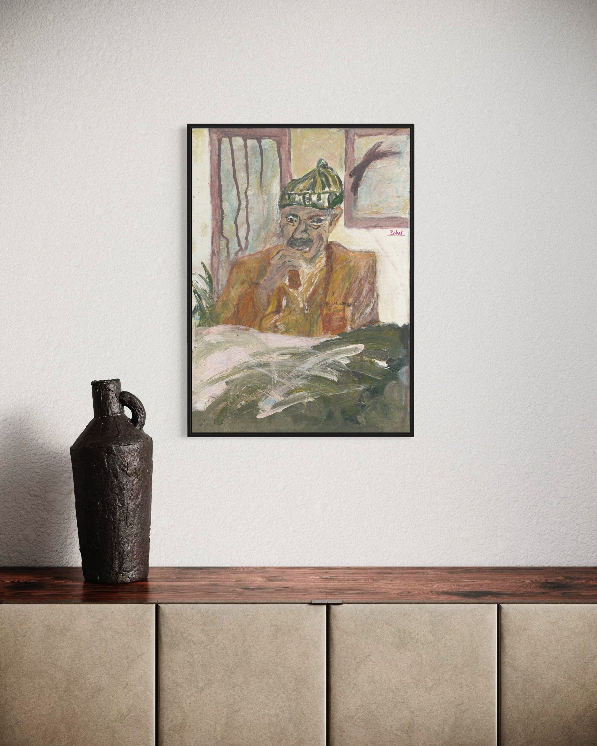 Framed artwork of a person with a green hat on a wall above a wooden shelf with a vase.