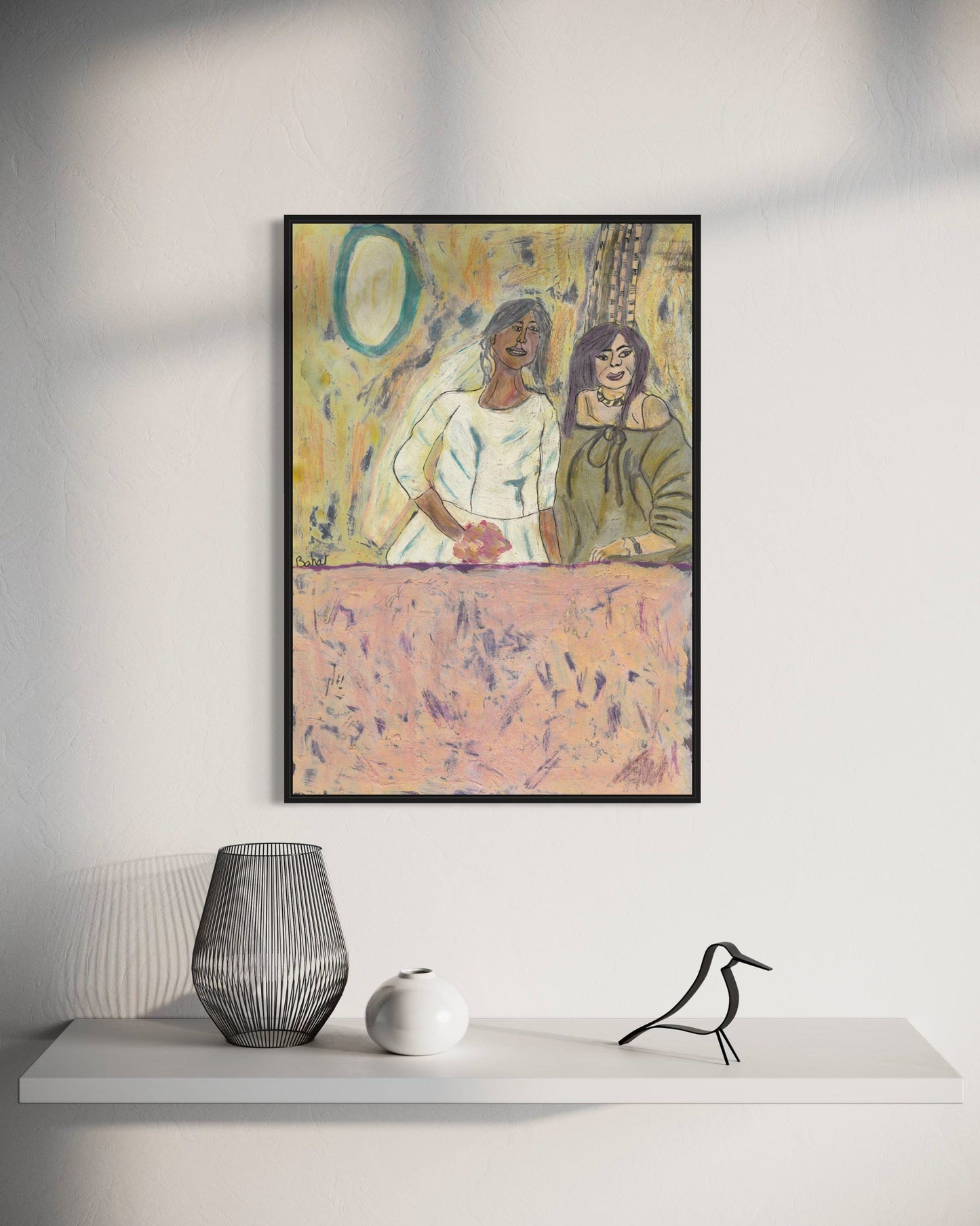 Framed artwork of two women sitting together on a table, with a vase and sculpture below on a white surface.
