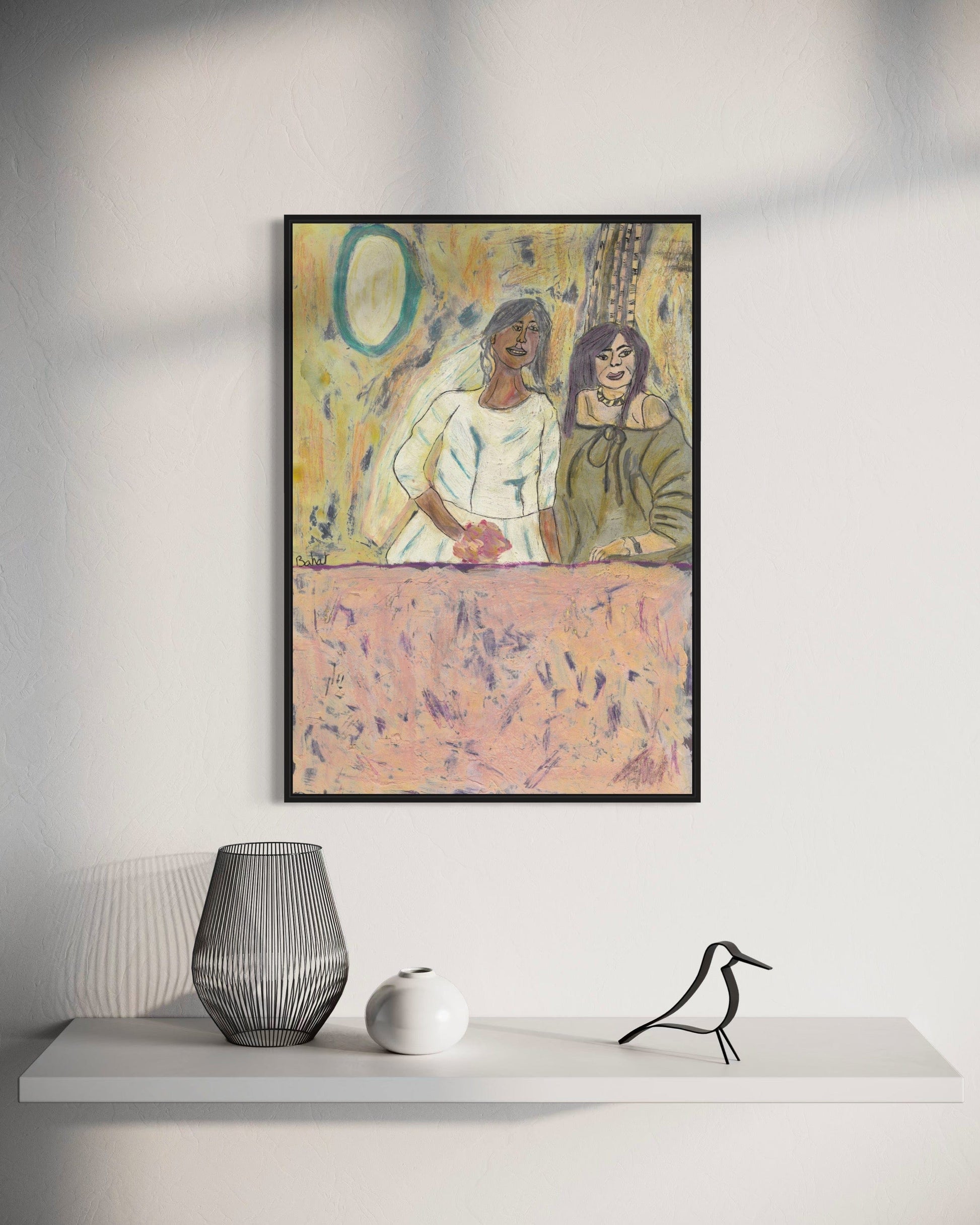 Framed artwork of two women sitting together on a table, with a vase and sculpture below on a white surface.