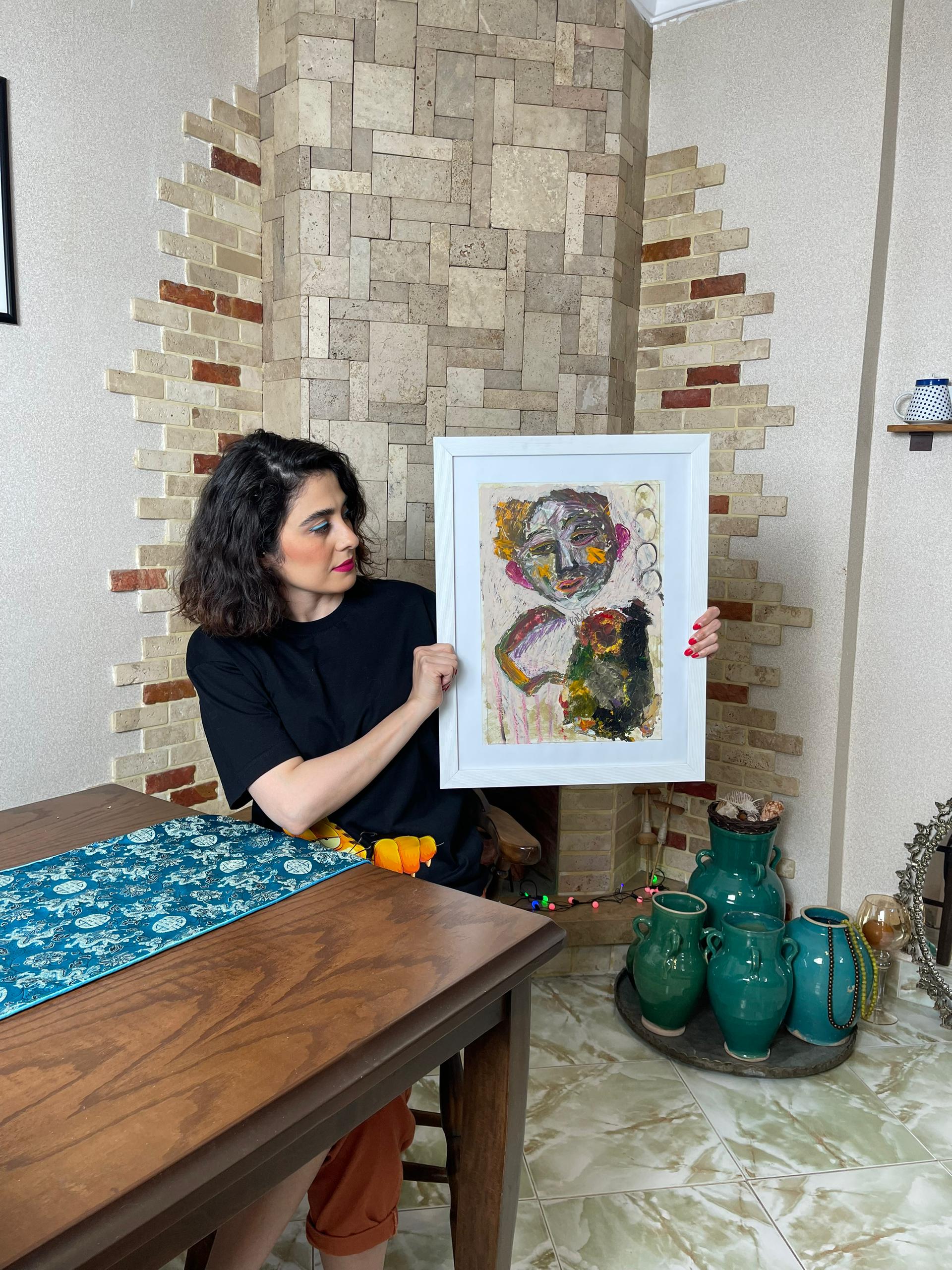 Woman holding a framed artwork in a room with decorative elements.