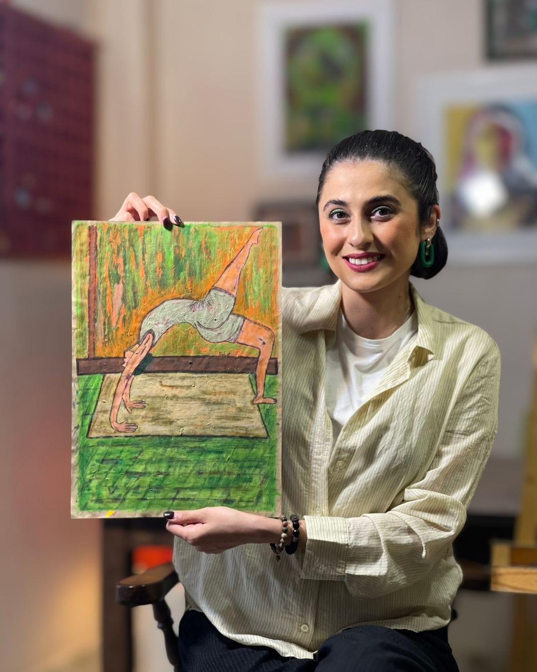 Woman holding a colorful painting of a dancer in an indoor setting